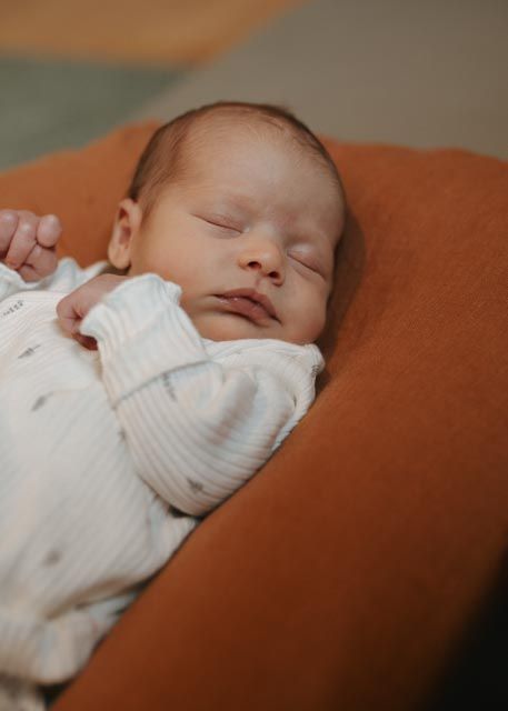 Serene newborn baby sleeping peacefully on rust-colored pillow wearing white onesie during newborn session.