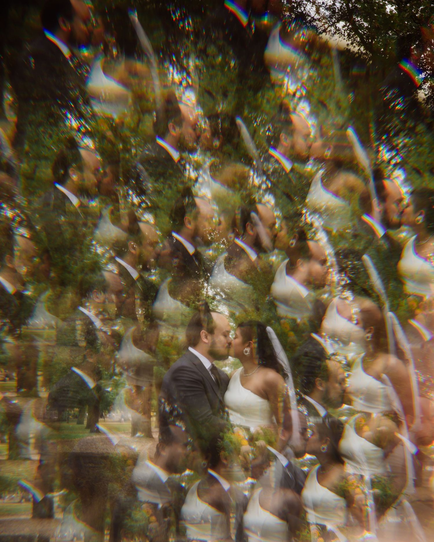 Artistic multiple-exposure wedding photo of bride and groom kissing among trees.