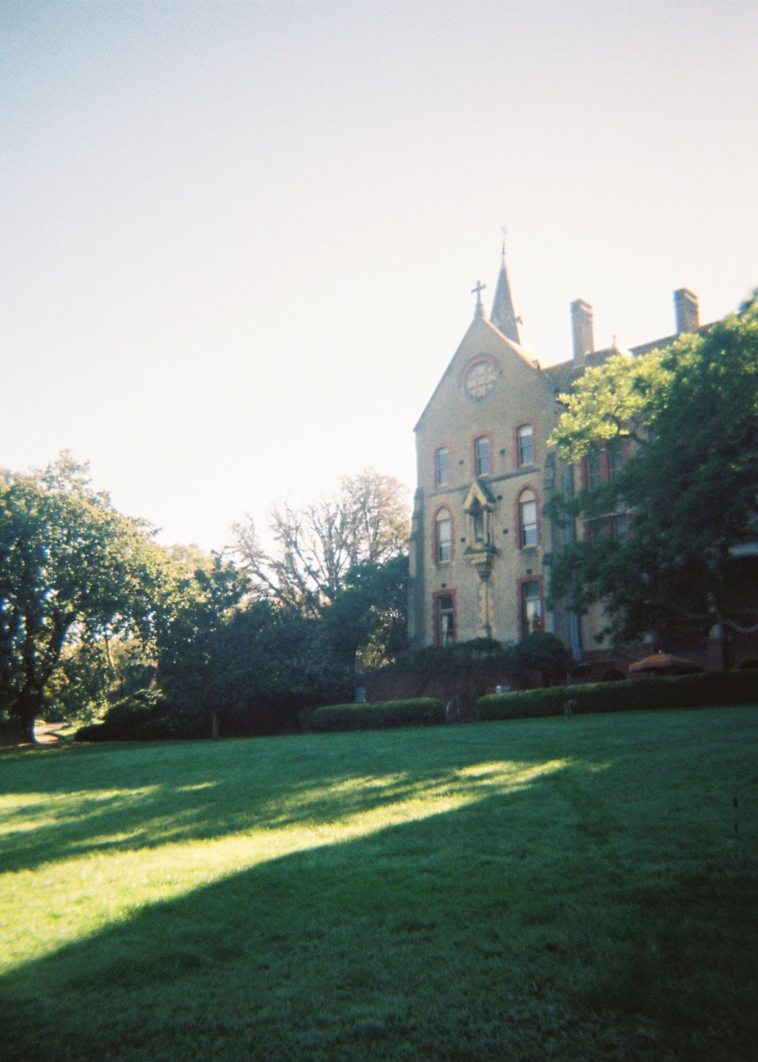 A historic Gothic-style stone building with a clock tower surrounded by green lawns and trees.