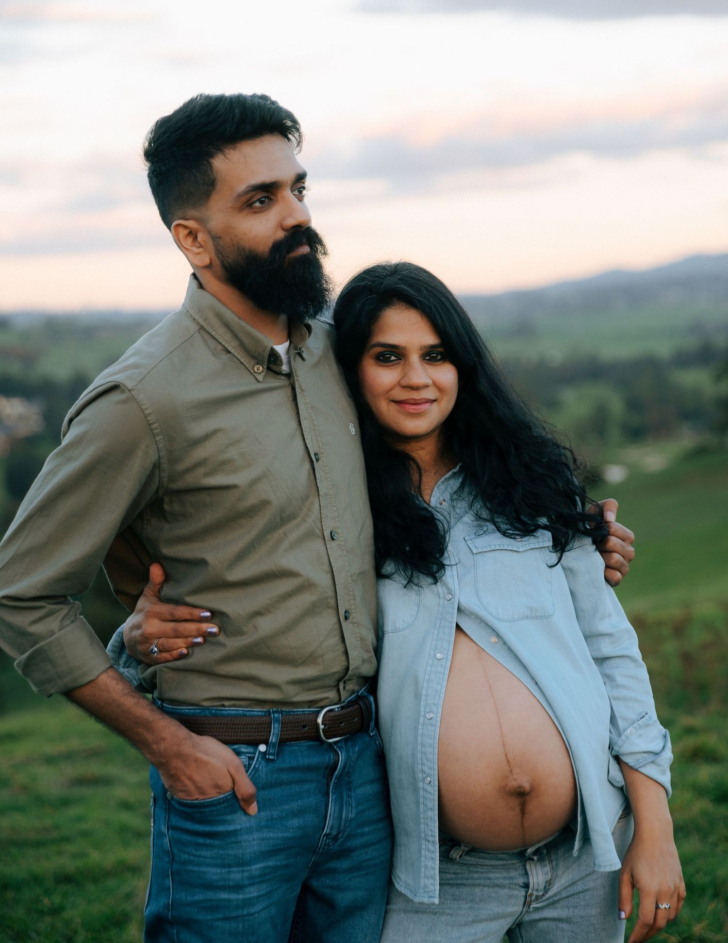 Bearded man embraces smiling pregnant partner during outdoor maternity portrait session.