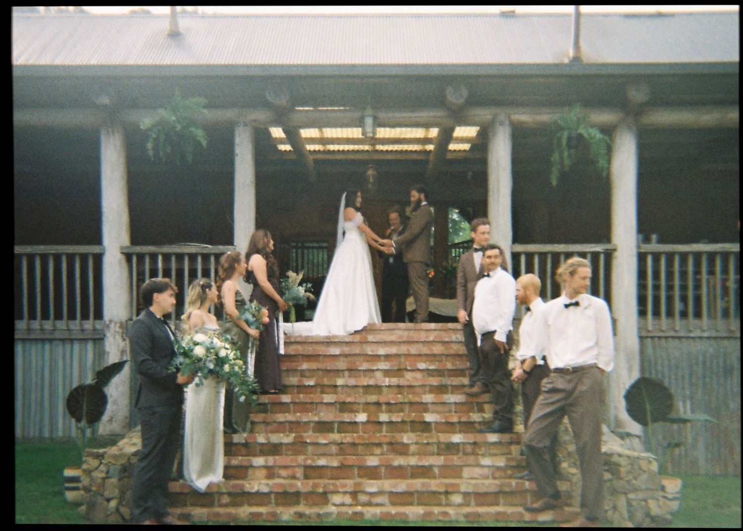 Wedding party gathered on brick steps of a rustic venue during outdoor ceremony.