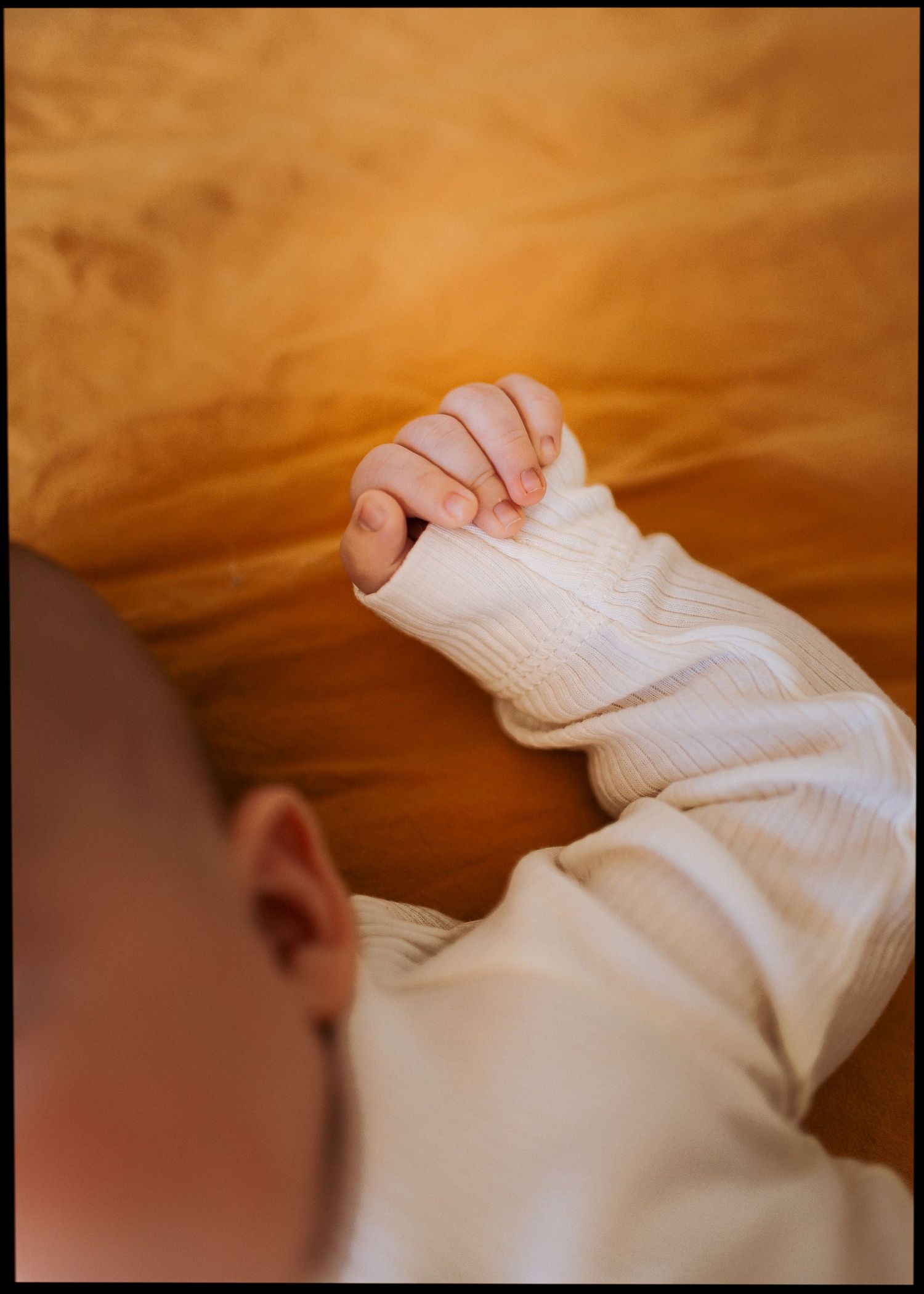Sleeping baby in a cream ribbed onesie rests on a golden yellow blanket with a tiny hand curled near the head.
