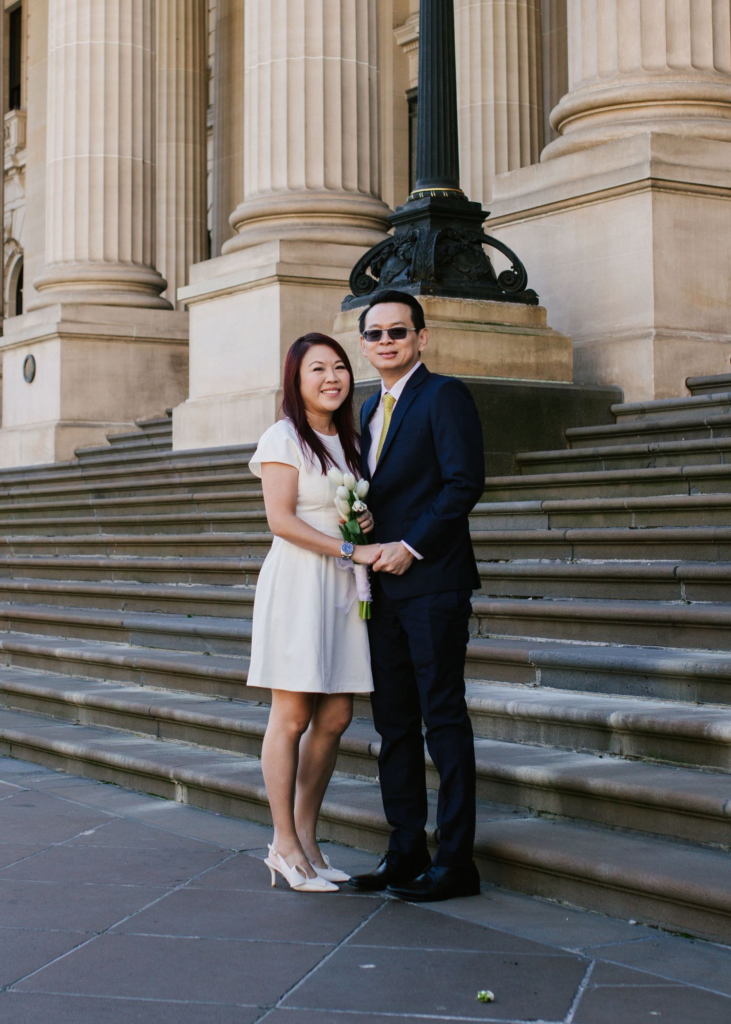 Asian couple posing on steps of grand neoclassical building with tall stone columns.
