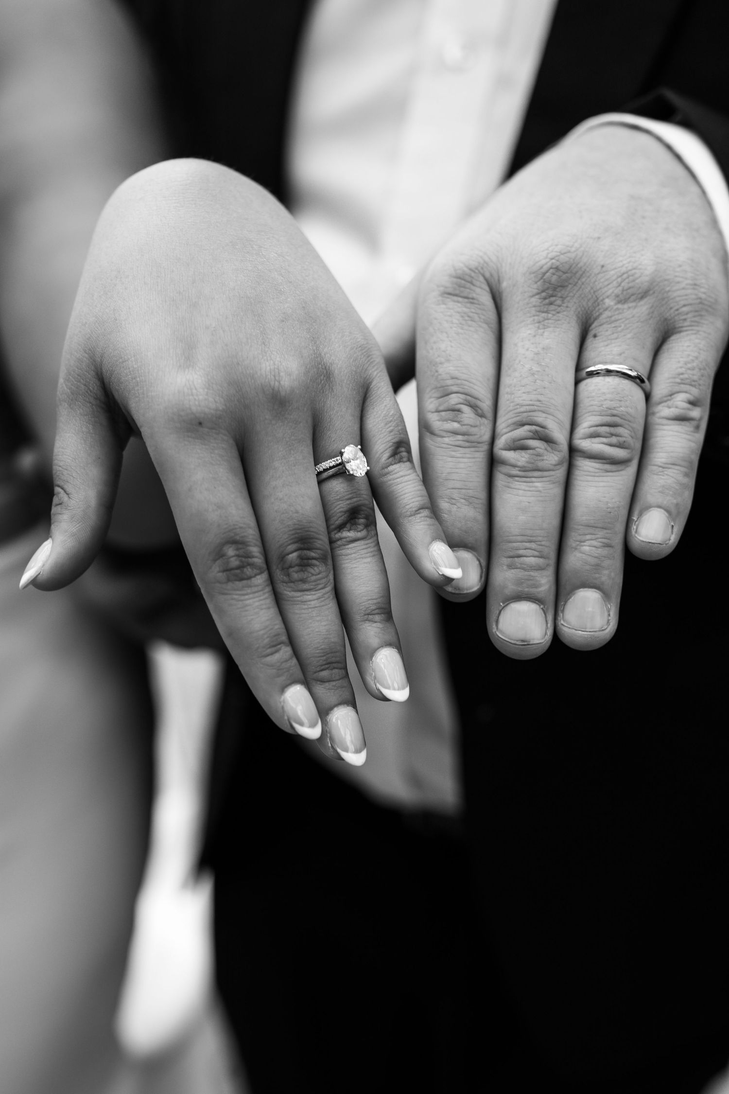Black and white close-up of newlyweds displaying wedding rings, bride wearing diamond engagement ring.