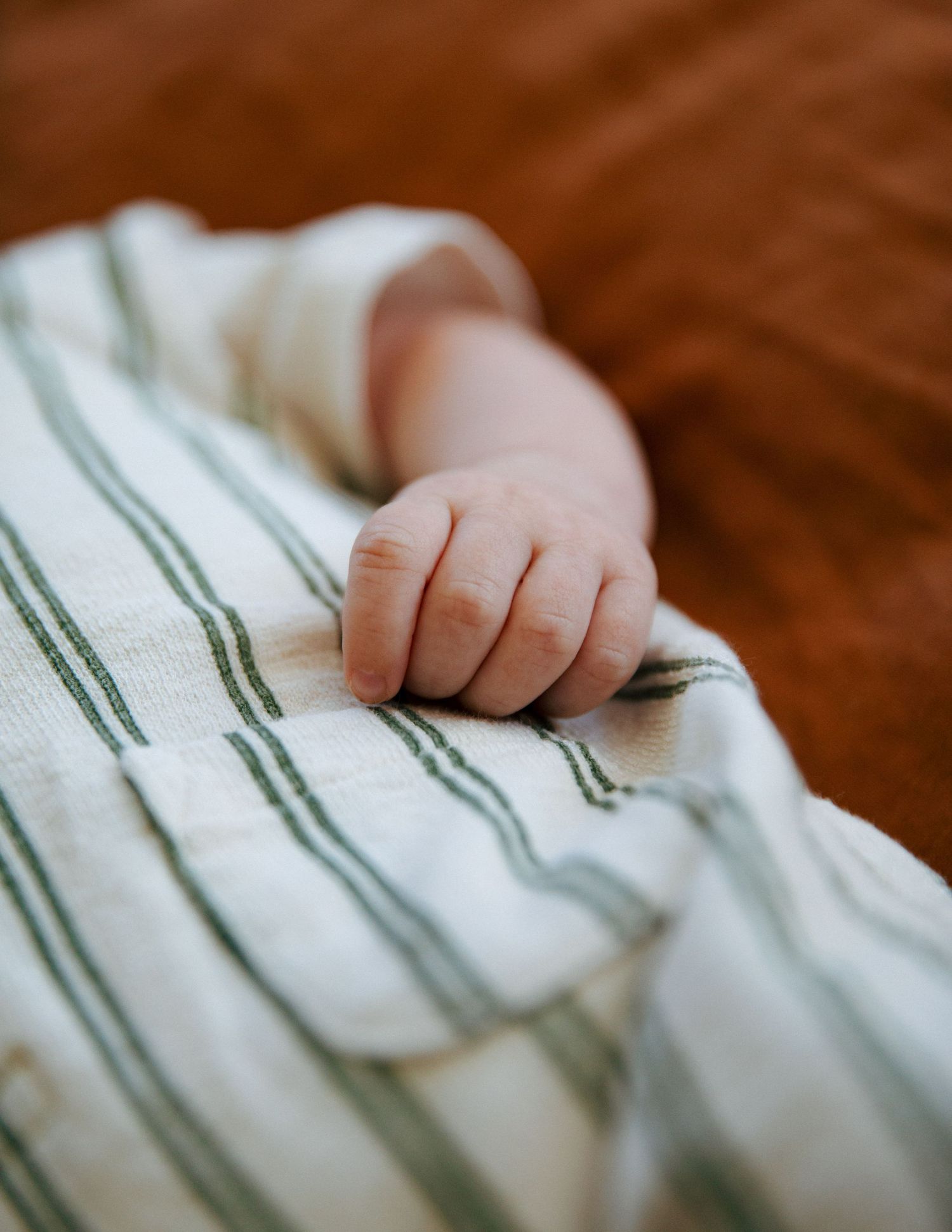 Newborn baby hand grasping a white and green striped swaddle blanket.