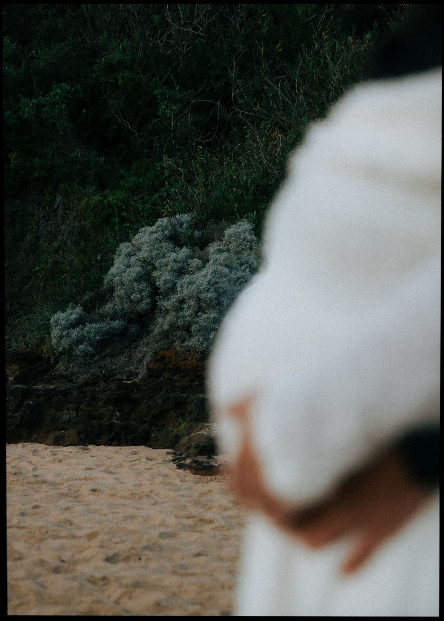 Artistic blurred maternity photo focusing on pregnant belly in white dress on sandy beach.
