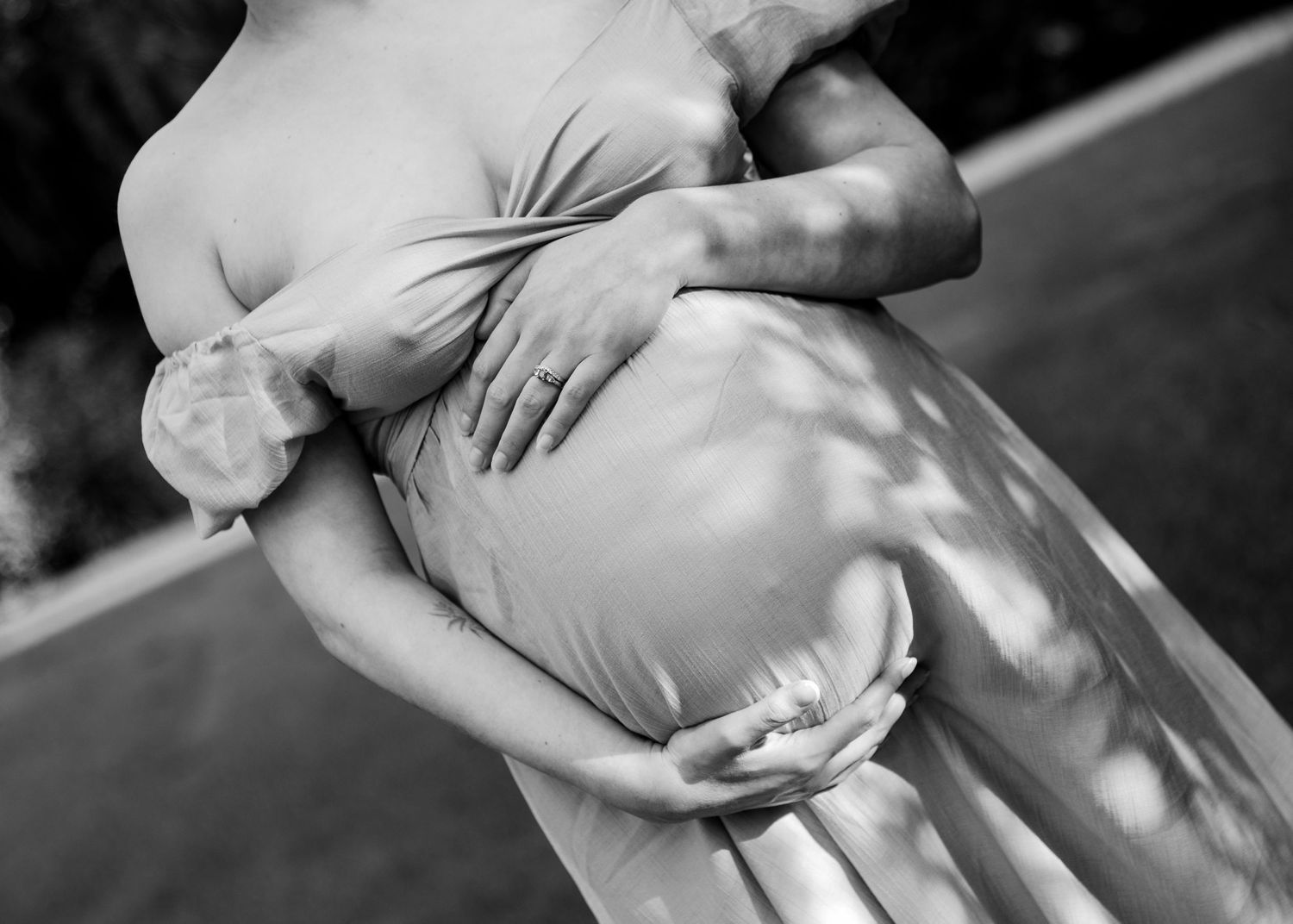 Black and white close-up of pregnant woman in flowing dress with partner embracing her baby bump.