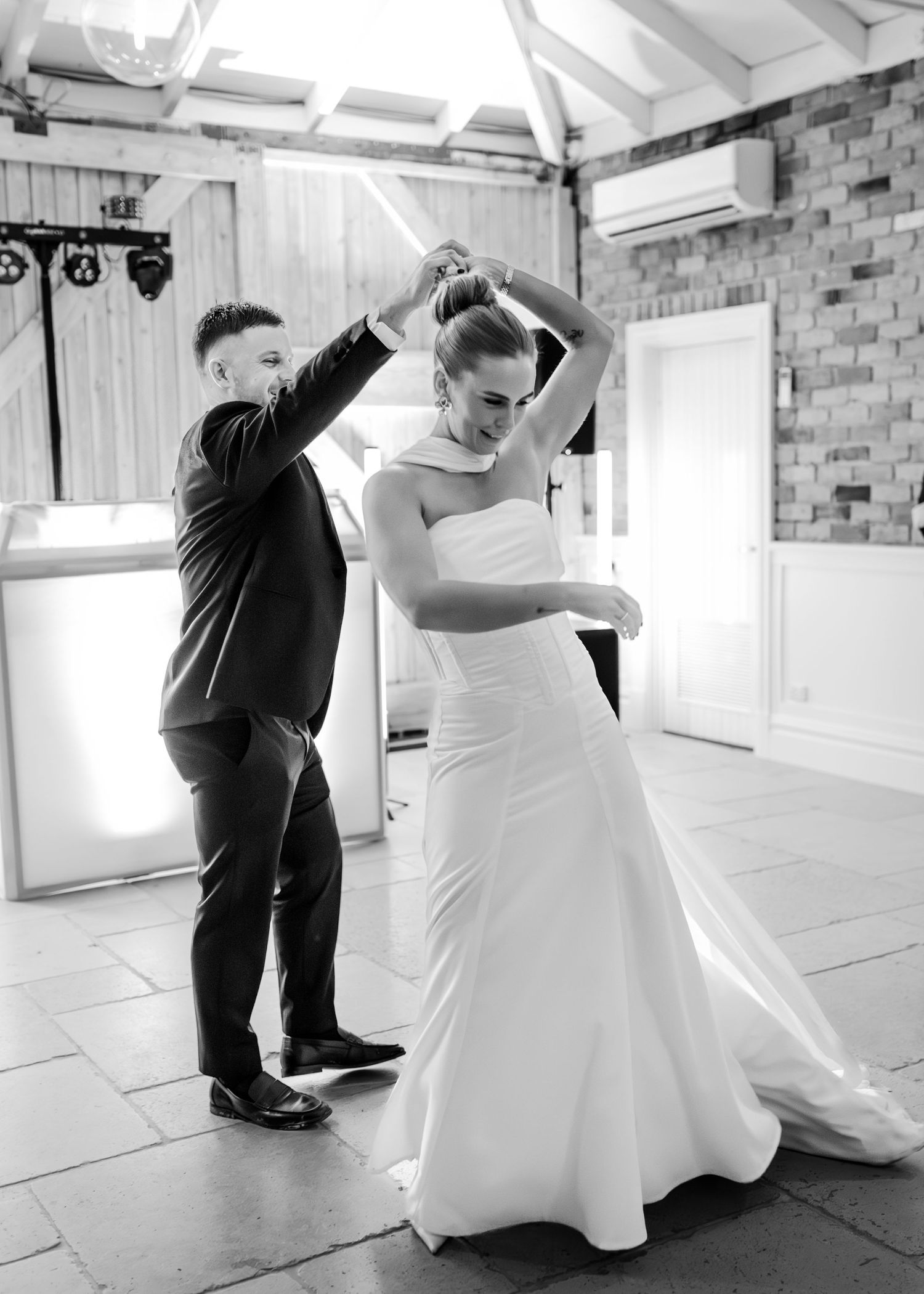 Bride and groom share their first dance, with groom spinning bride in elegant wedding gown in a rustic venue.