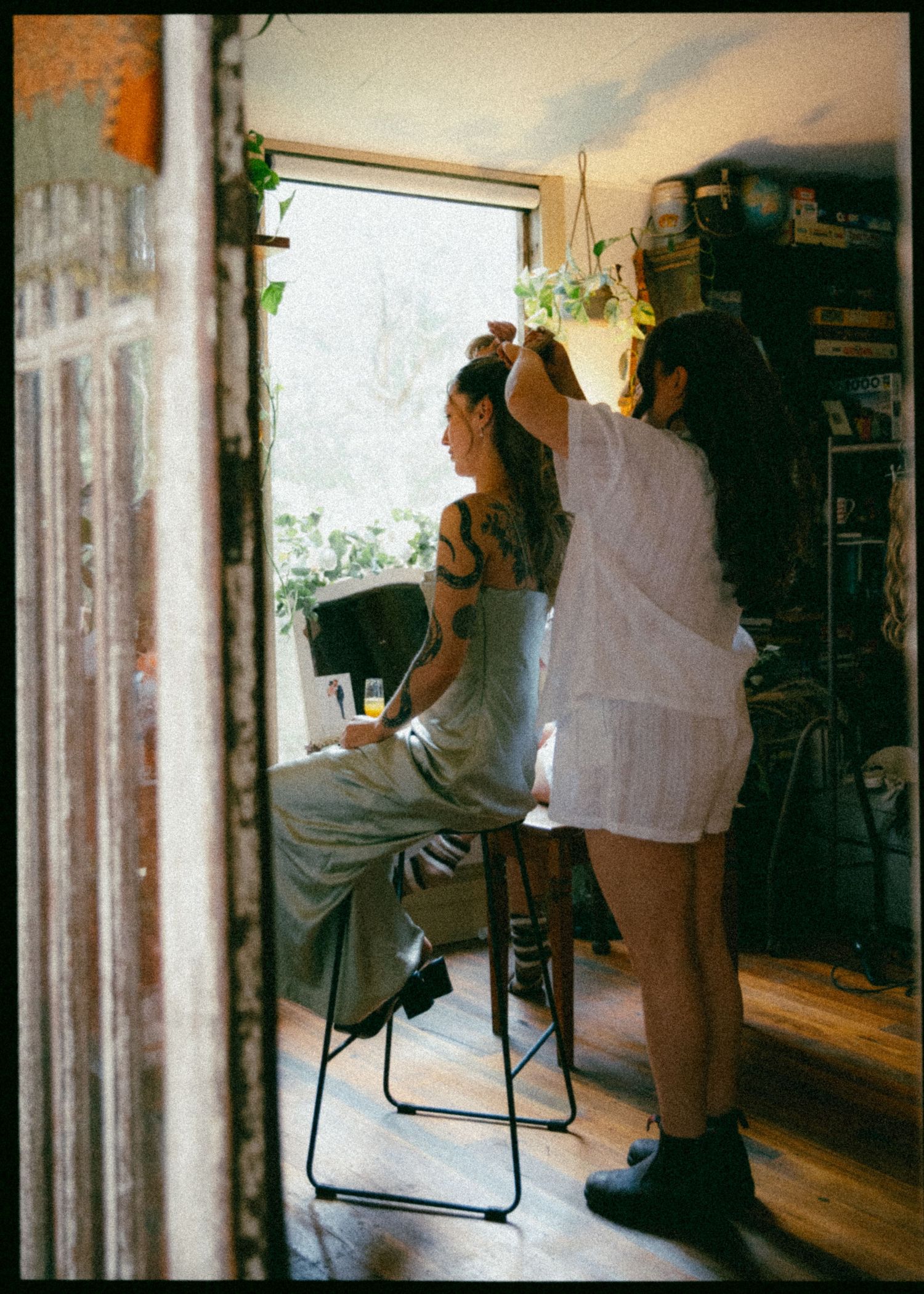 Bridesmaid getting hair styled by another woman near a bright window in a cozy room.