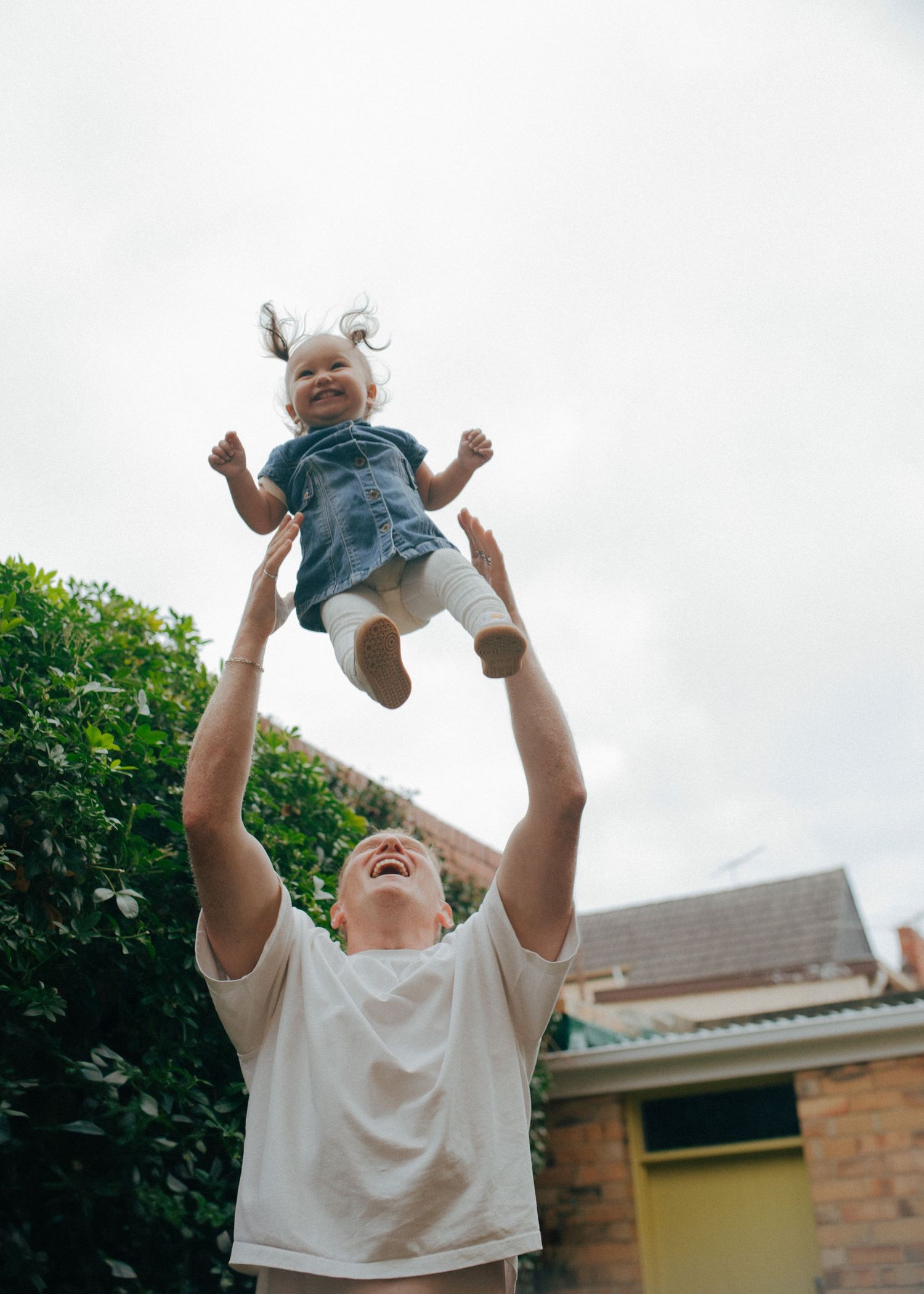 Laughing father joyfully tosses smiling baby girl into the air outdoors.