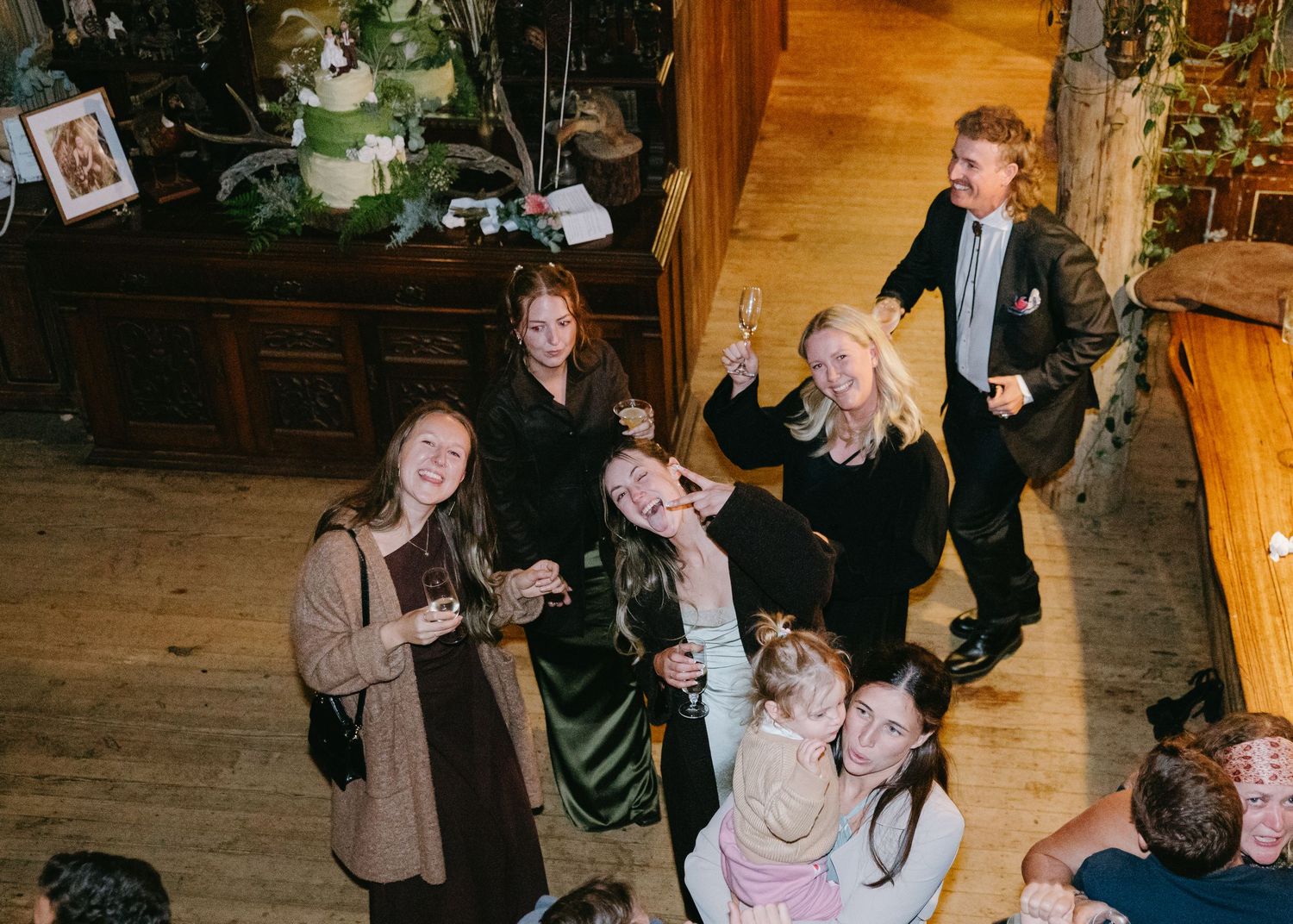 Group of friends smiling and raising glasses at an indoor party celebration.