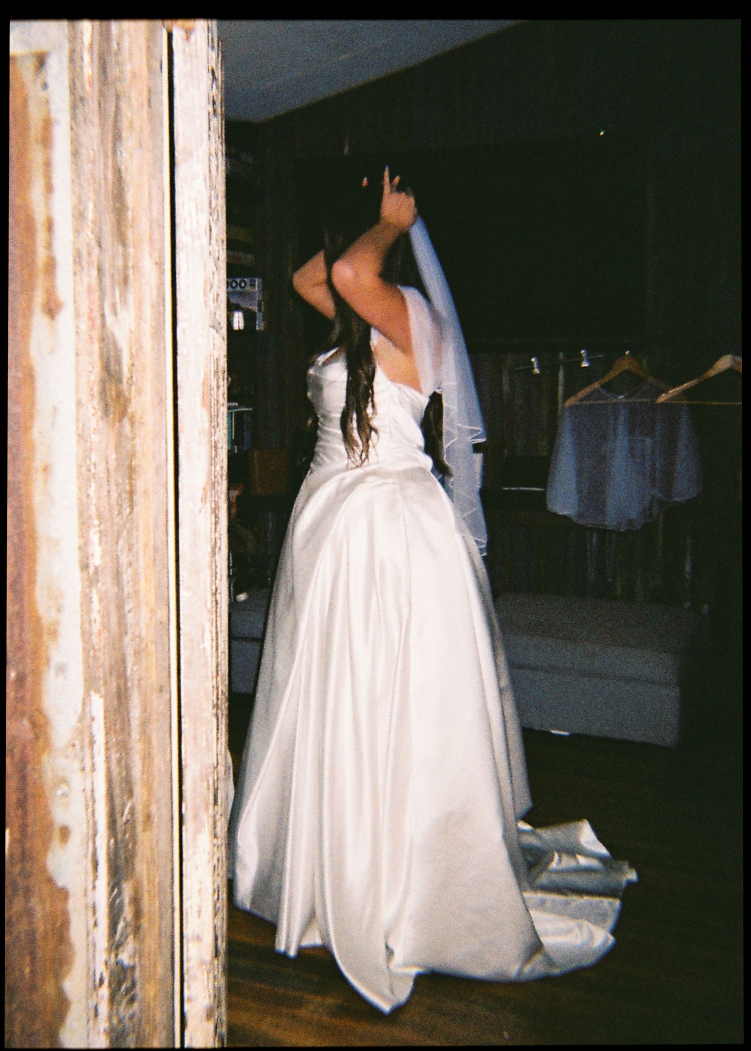 Bride in a white strapless ballgown with veil adjusting her hair in a rustic wooden barn dressing room.