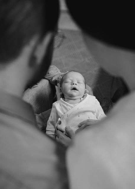 Black and white photo of newborn baby yawning peacefully while being held by parent during newborn shoot.
