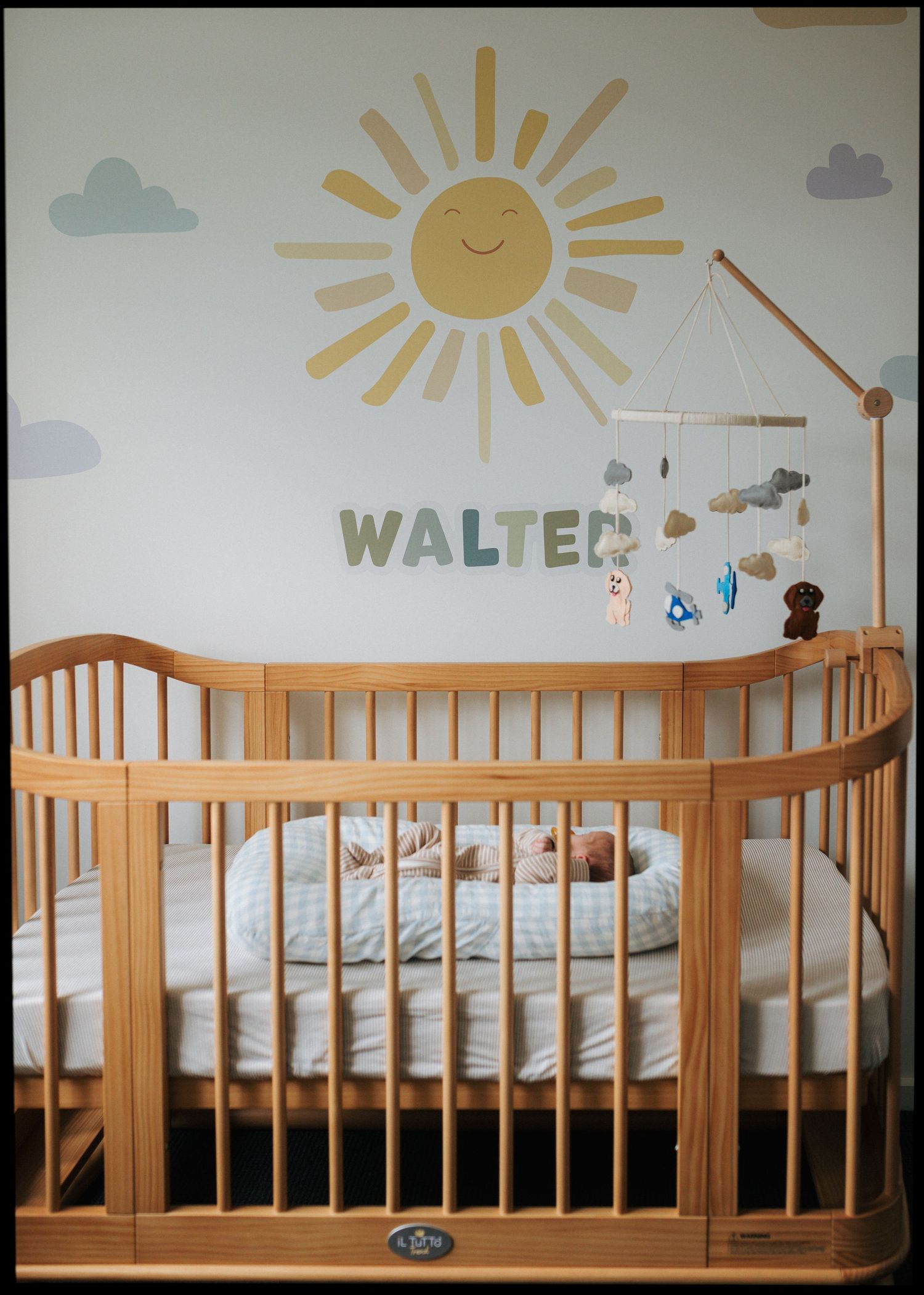 Wooden baby crib in nursery with sun mural and name WALTER on the wall.