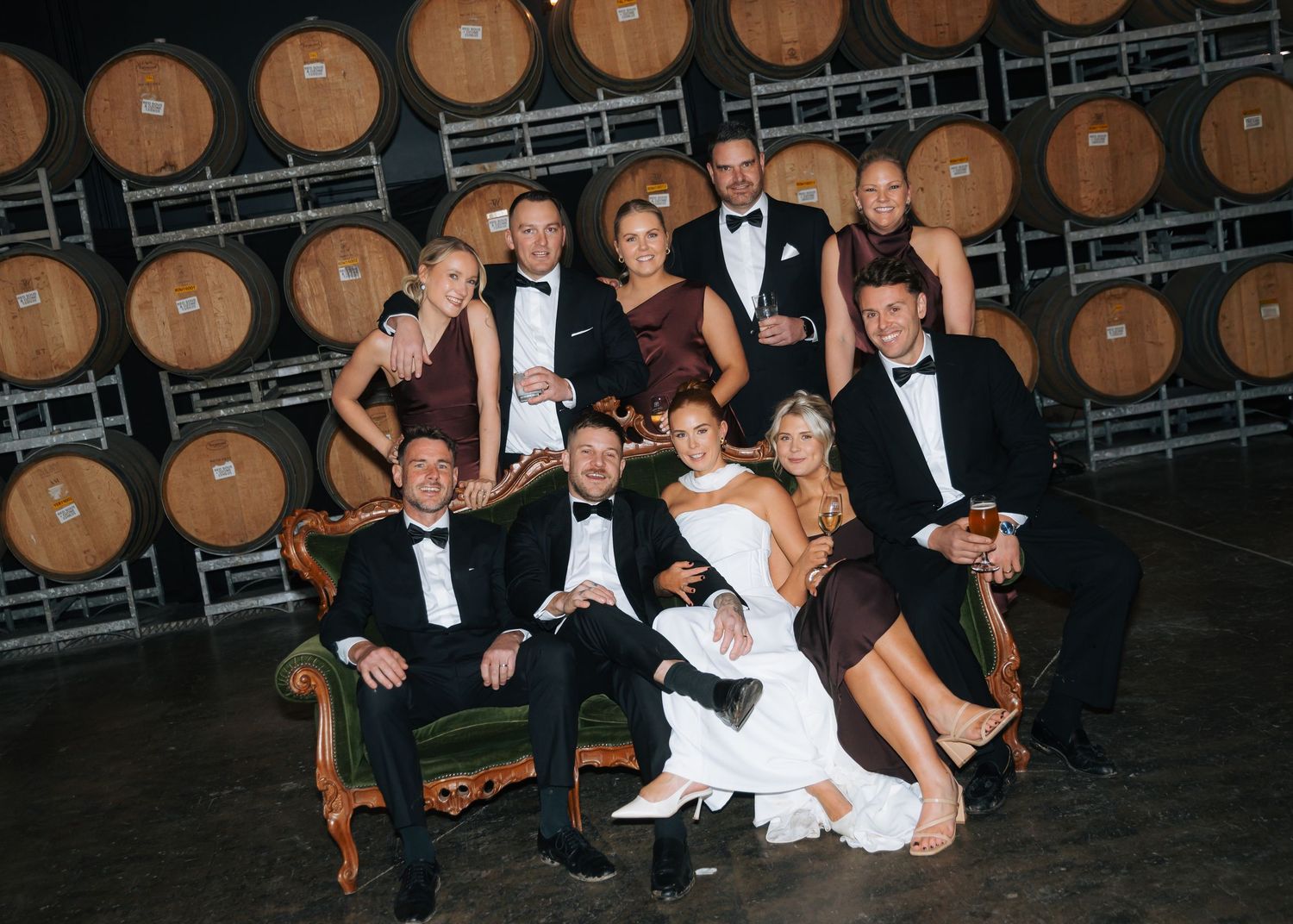 Wedding party posing together in front of wine barrel wall.