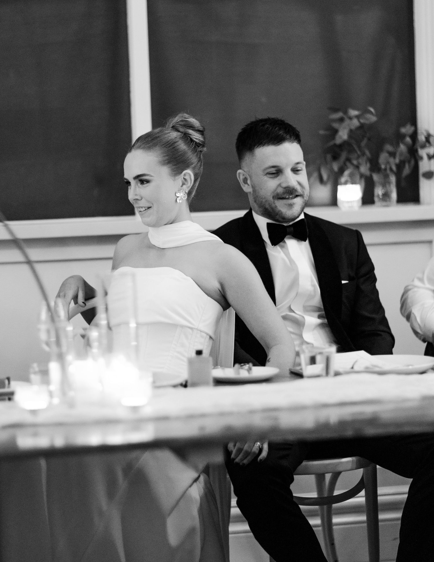 Black and white photo of smiling bride and groom seated at wedding reception table with candles.