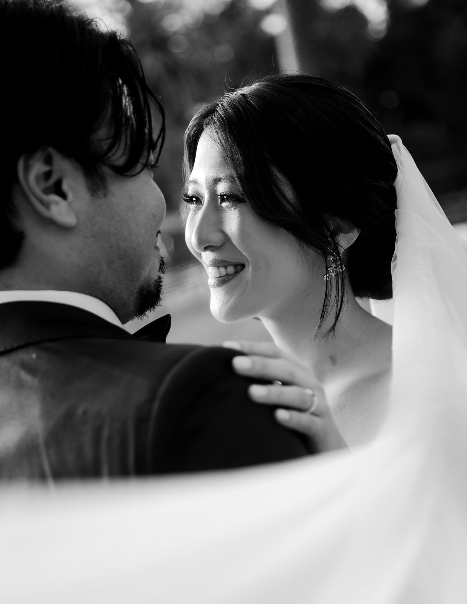 Black and white close-up of a smiling bride in a veil looking lovingly at her groom on their wedding day.