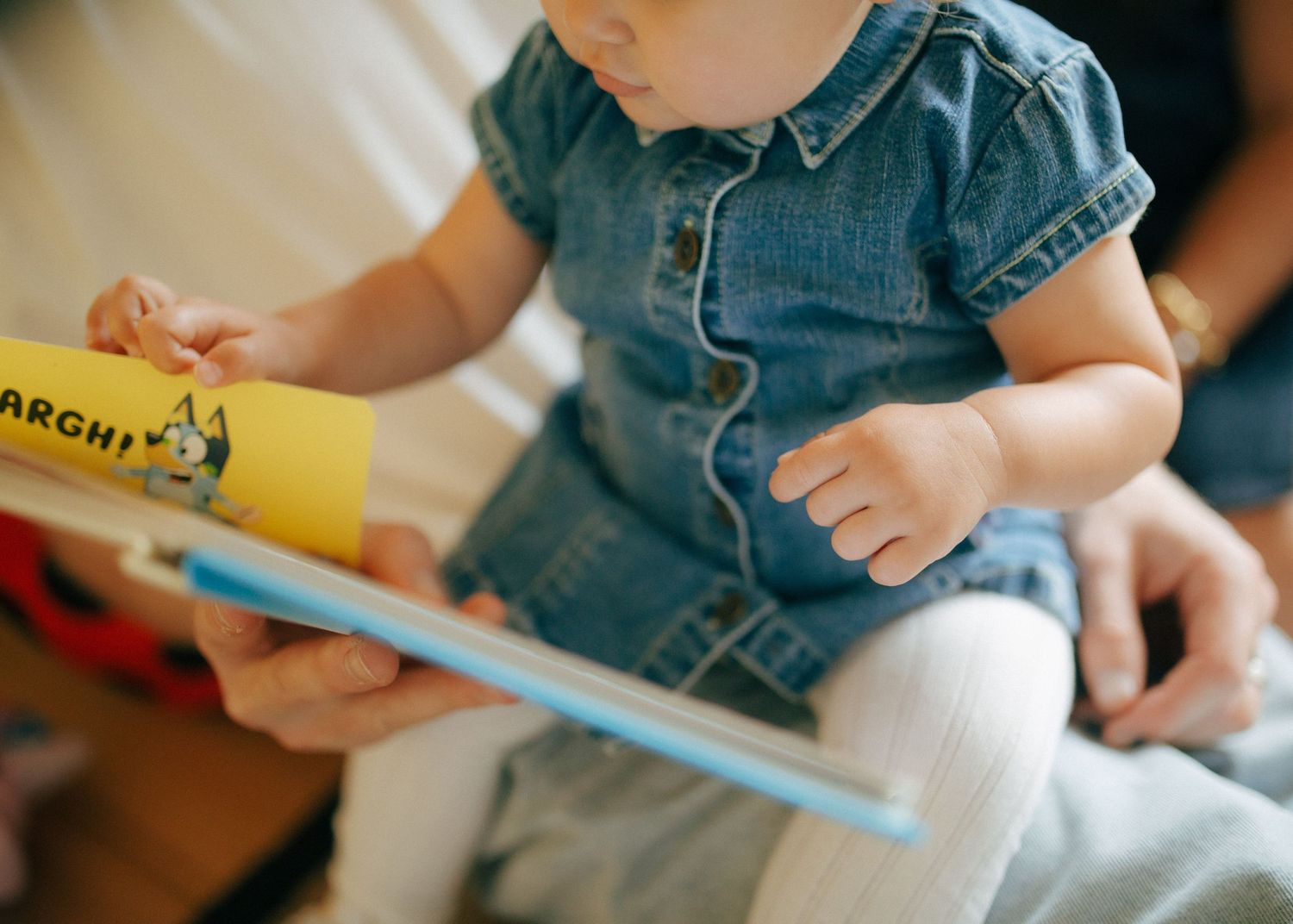 Close-up of a baby in a denim outfit reading a colorful picture book.