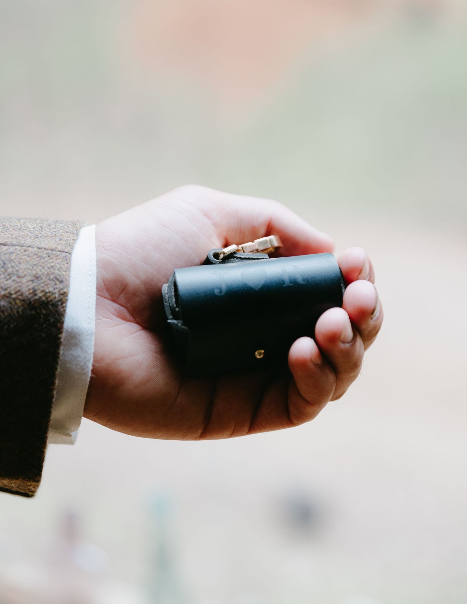 Close-up of groom holding a black leather ring box with gold wedding rings on his palm.