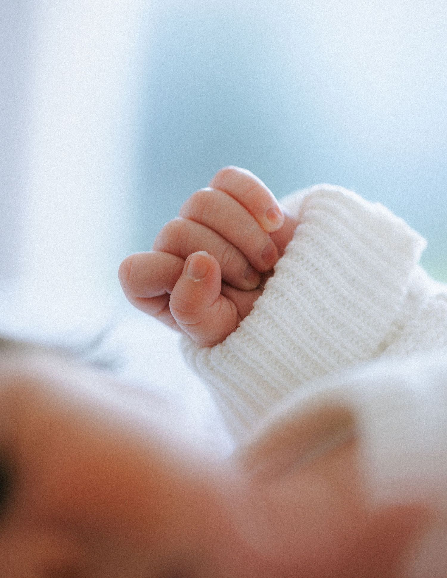 Close-up of a newborn baby's tiny hand clutching a white knit sleeve.