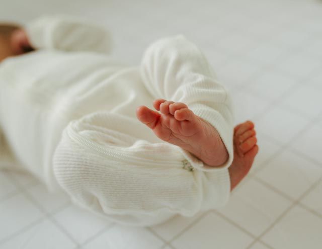Tiny newborn baby feet peeking out of white knit outfit while lying down.