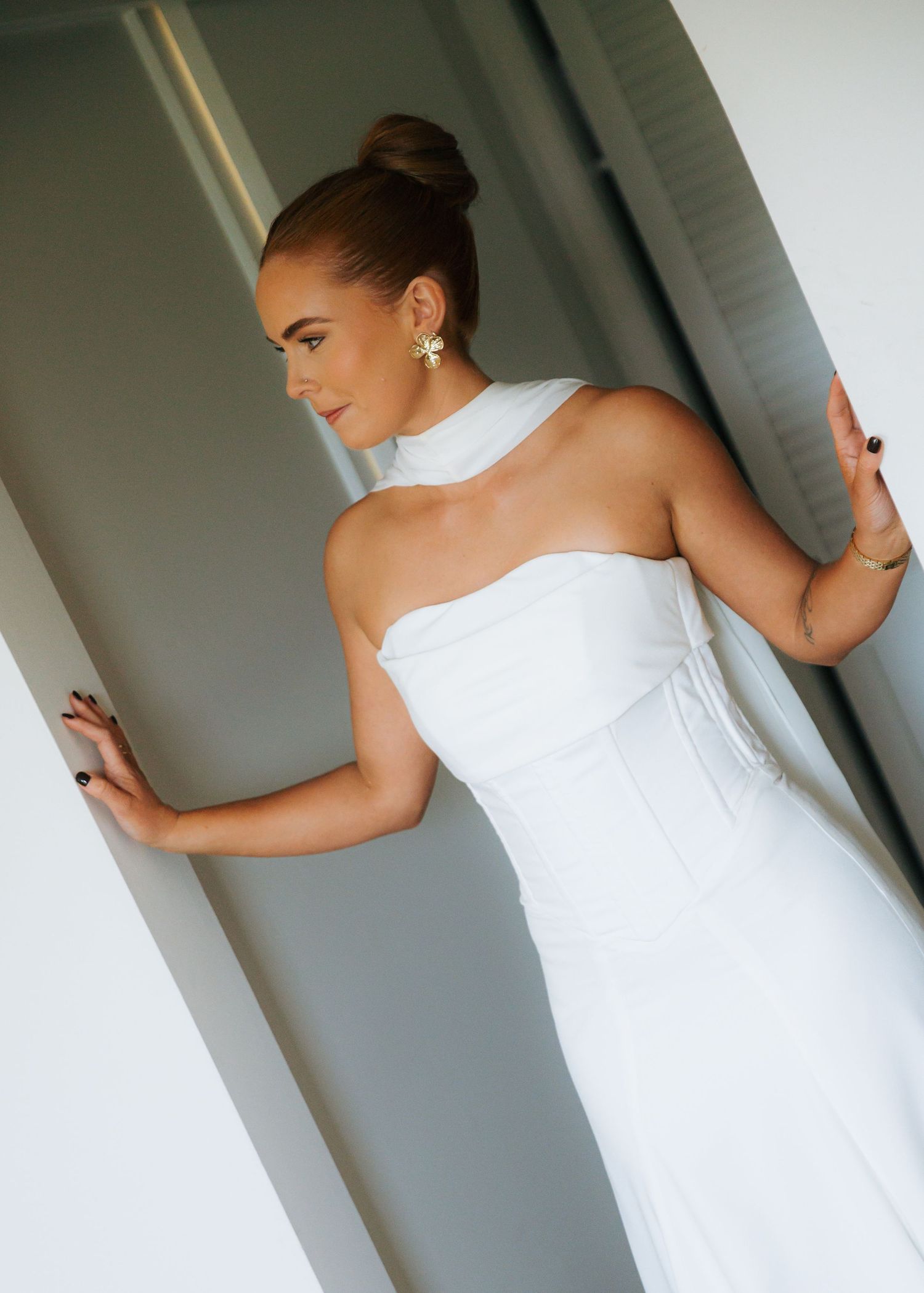 Bride in white strapless corset wedding gown with halter detail poses in doorway.