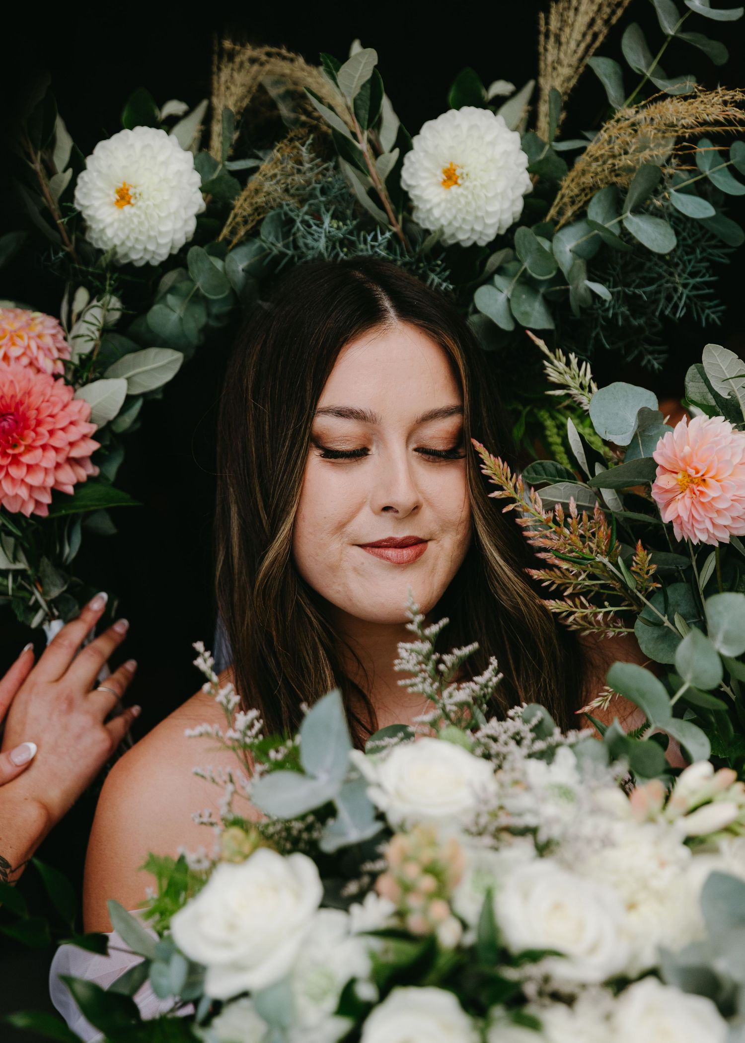 Beautiful bride surrounded by lush floral arrangement of dahlias, roses, and eucalyptus greenery.