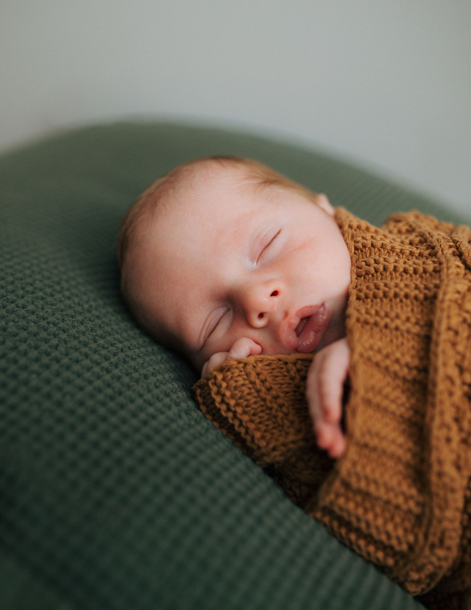 Peaceful newborn baby sleeping soundly wrapped in a warm mustard knit blanket on green cushion.