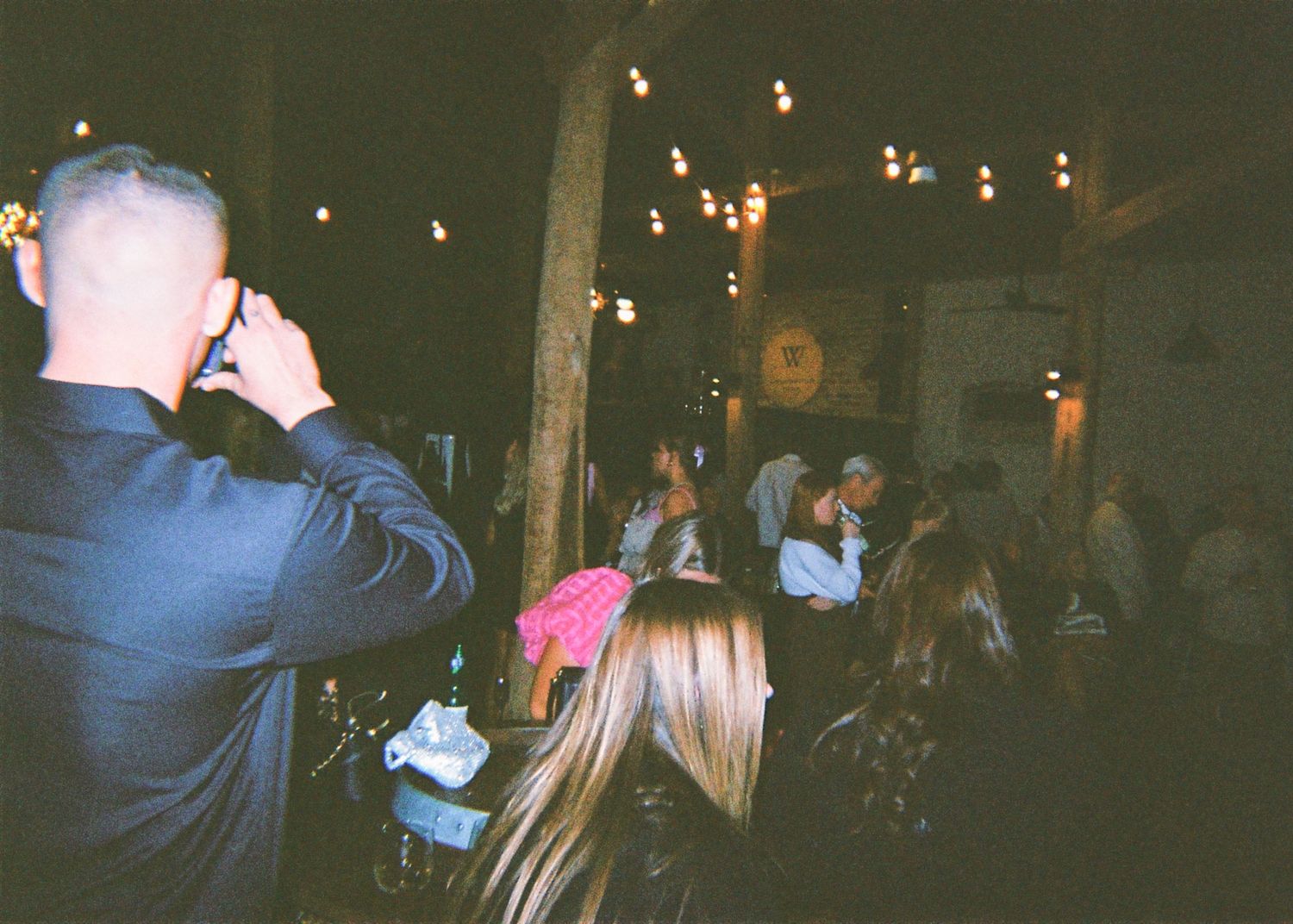 Guests mingling at a warmly lit rustic wedding reception venue with string lights overhead.