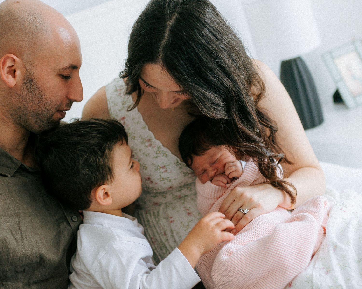 Loving family moment with parents and toddler boy gazing at newborn baby wrapped in pink blanket.