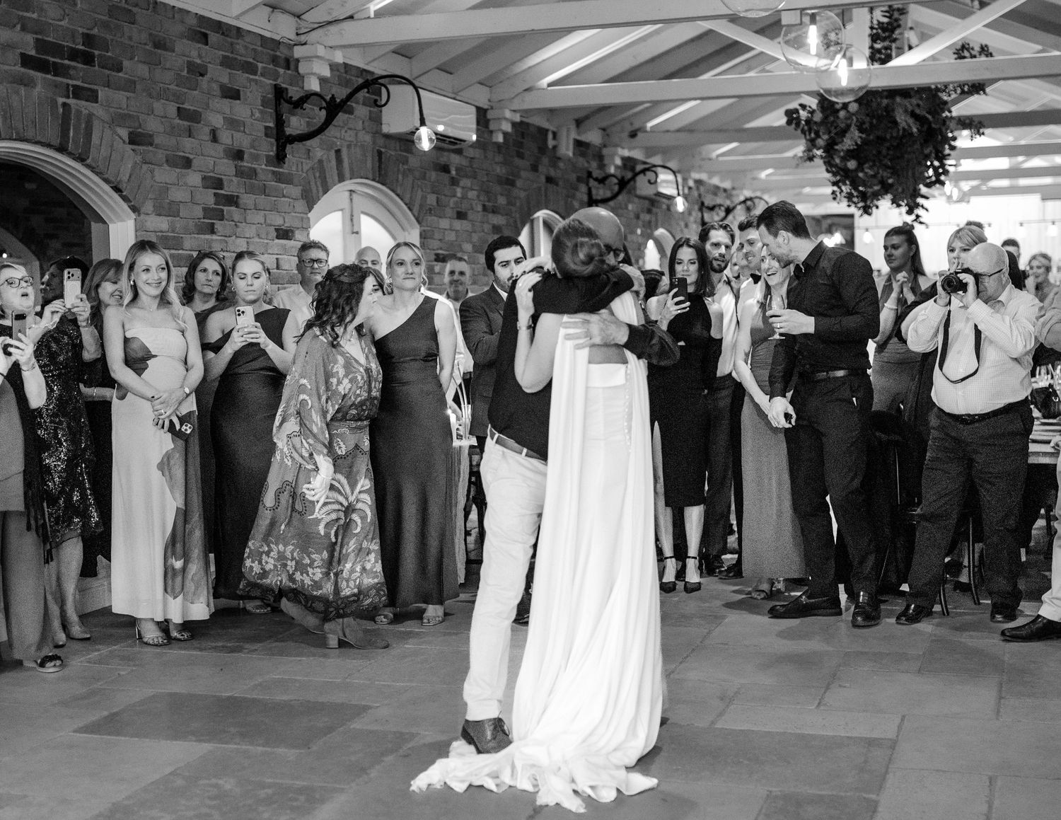 Bride and groom share first dance at wedding reception while guests watch and celebrate in elegant stone venue.