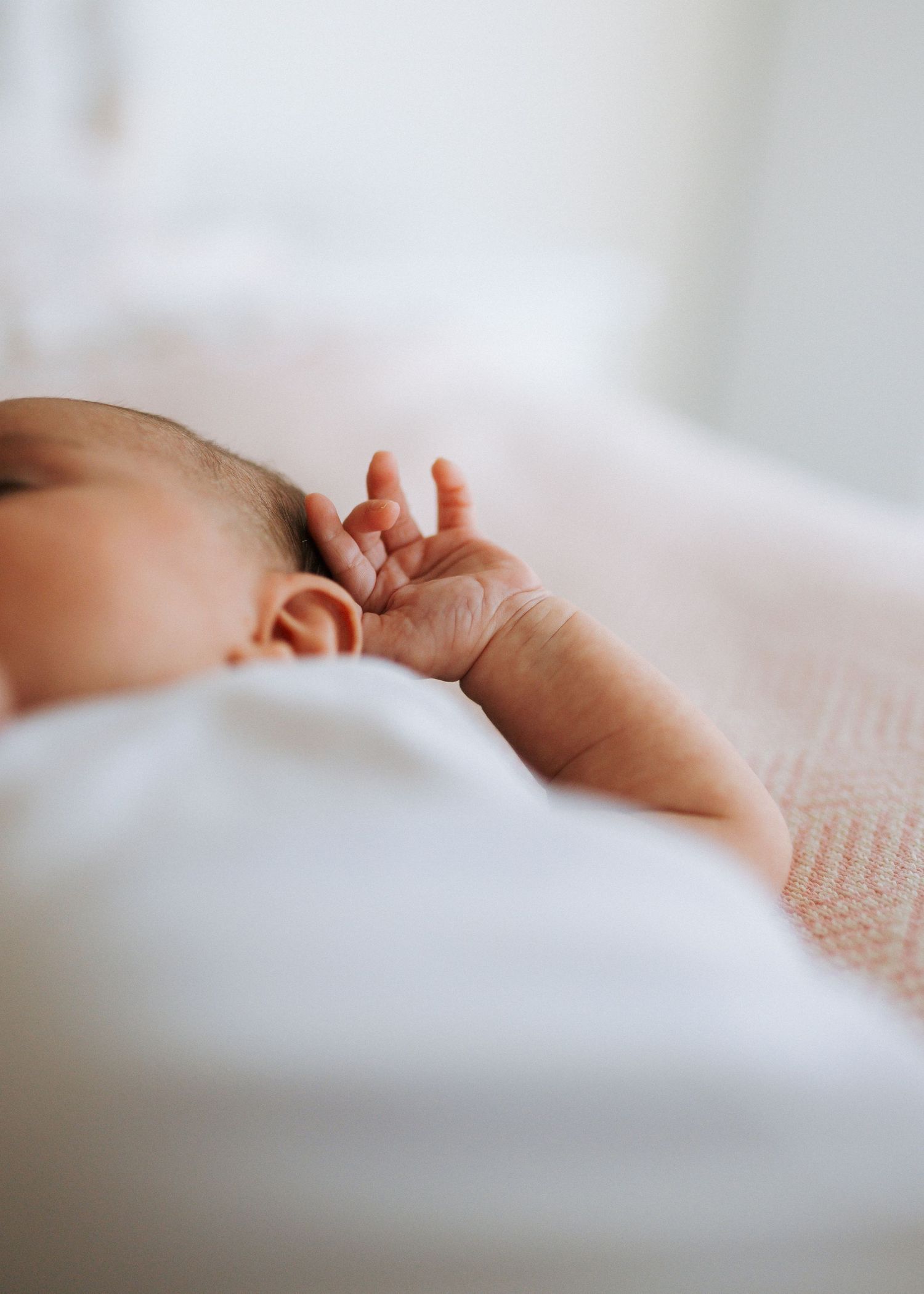 Close-up of a sleeping newborns tiny hand resting on a white blanket.