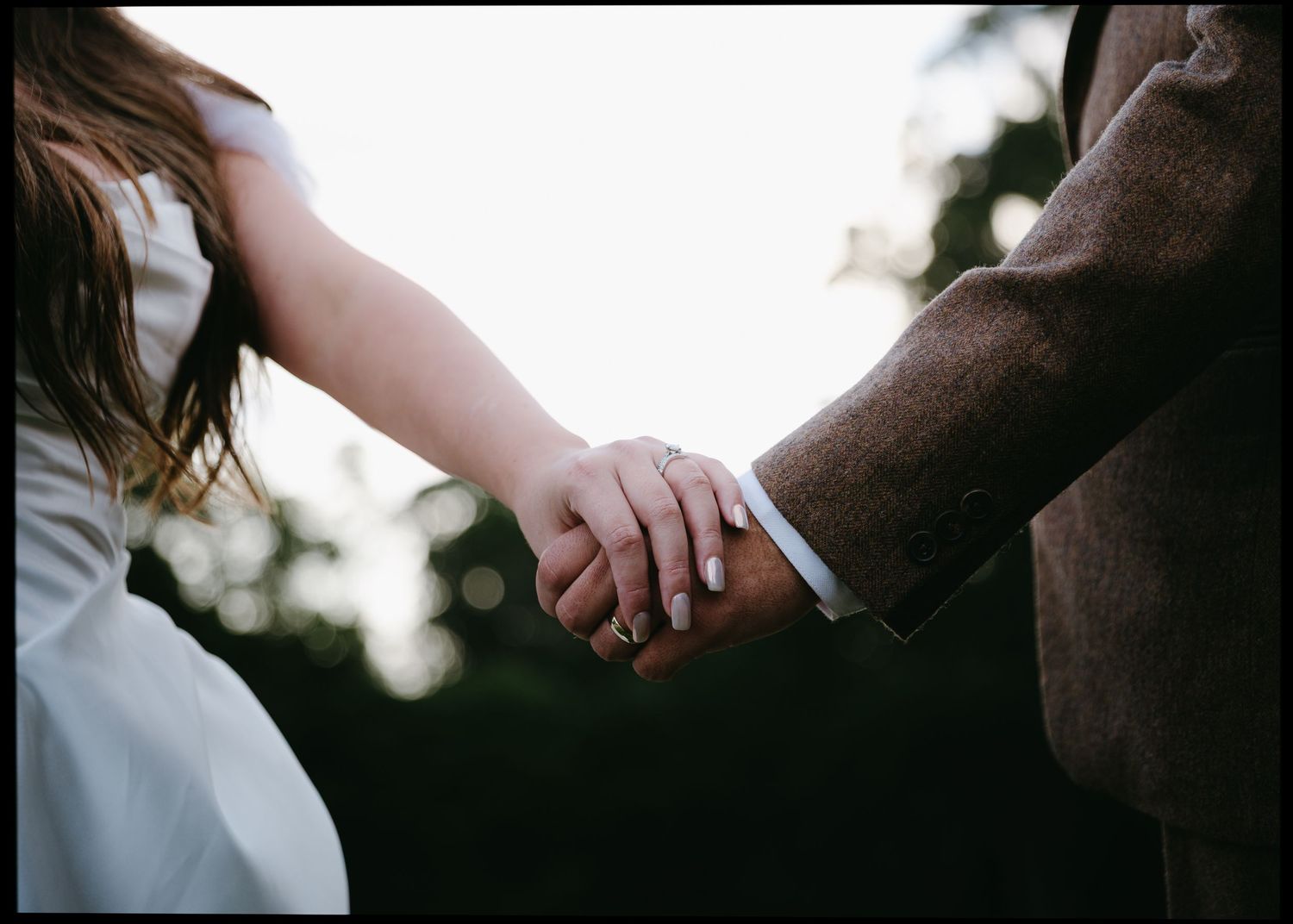 Bride and groom hold hands at sunset in romantic backlit photo.