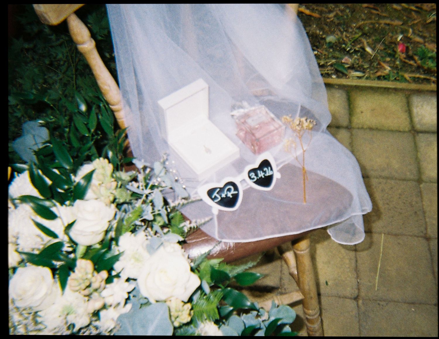 Wedding ceremony chair decorated with bridal veil, white bouquet, ring box, and heart signs.