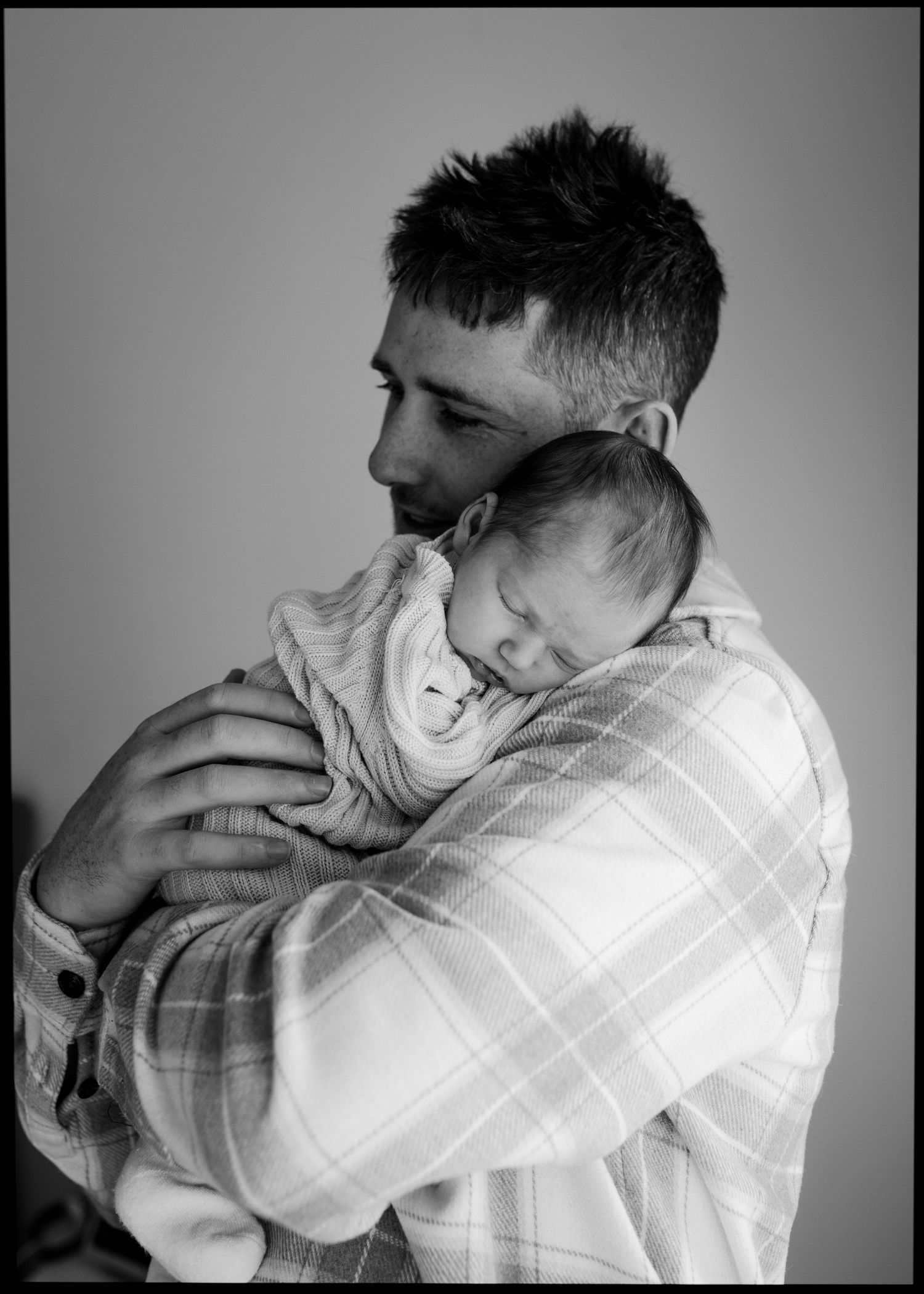 Black and white photo of father holding sleeping newborn baby against his chest.