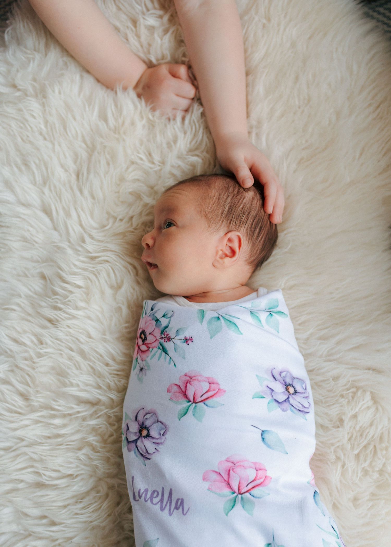 Parent gently touching newborn baby's head swaddled in floral blanket on fur rug.