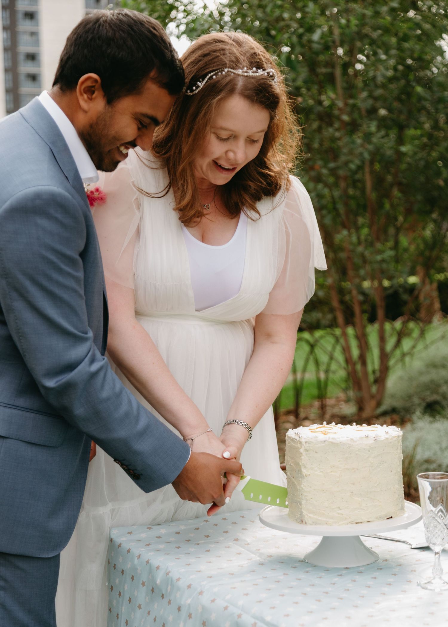 Bride and groom cut white wedding cake together at outdoor garden reception.