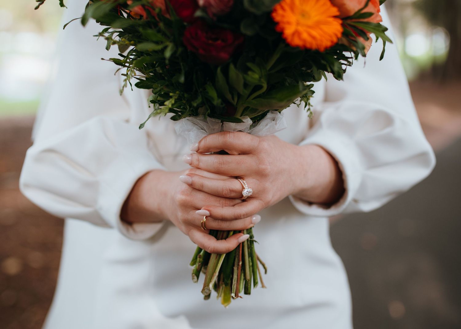 Close-up of bride holding vibrant orange and red wedding bouquet with elegant diamond engagement ring.