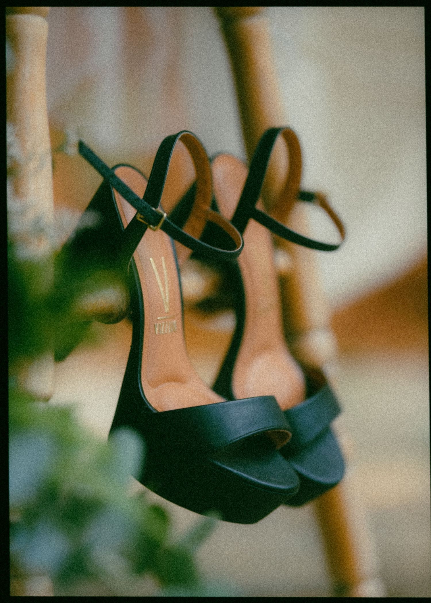 Elegant black platform heeled sandals hanging against a blurred natural background at a wedding.