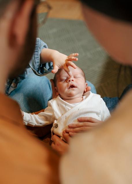 Newborn baby yawning while parent gently touches head during tender at-home newborn photography session.