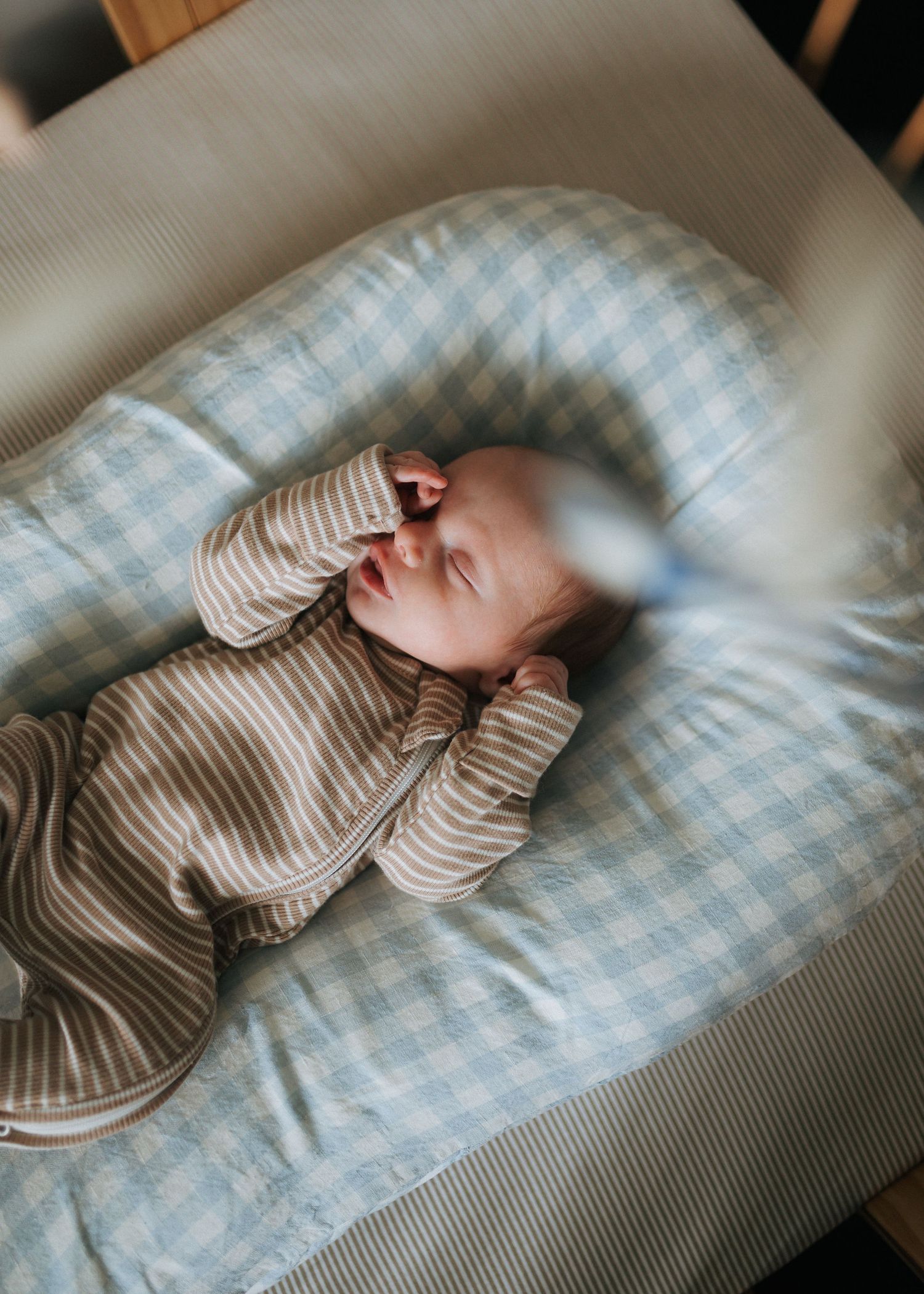Newborn baby in striped onesie lying awake in a soft blue gingham baby lounger.