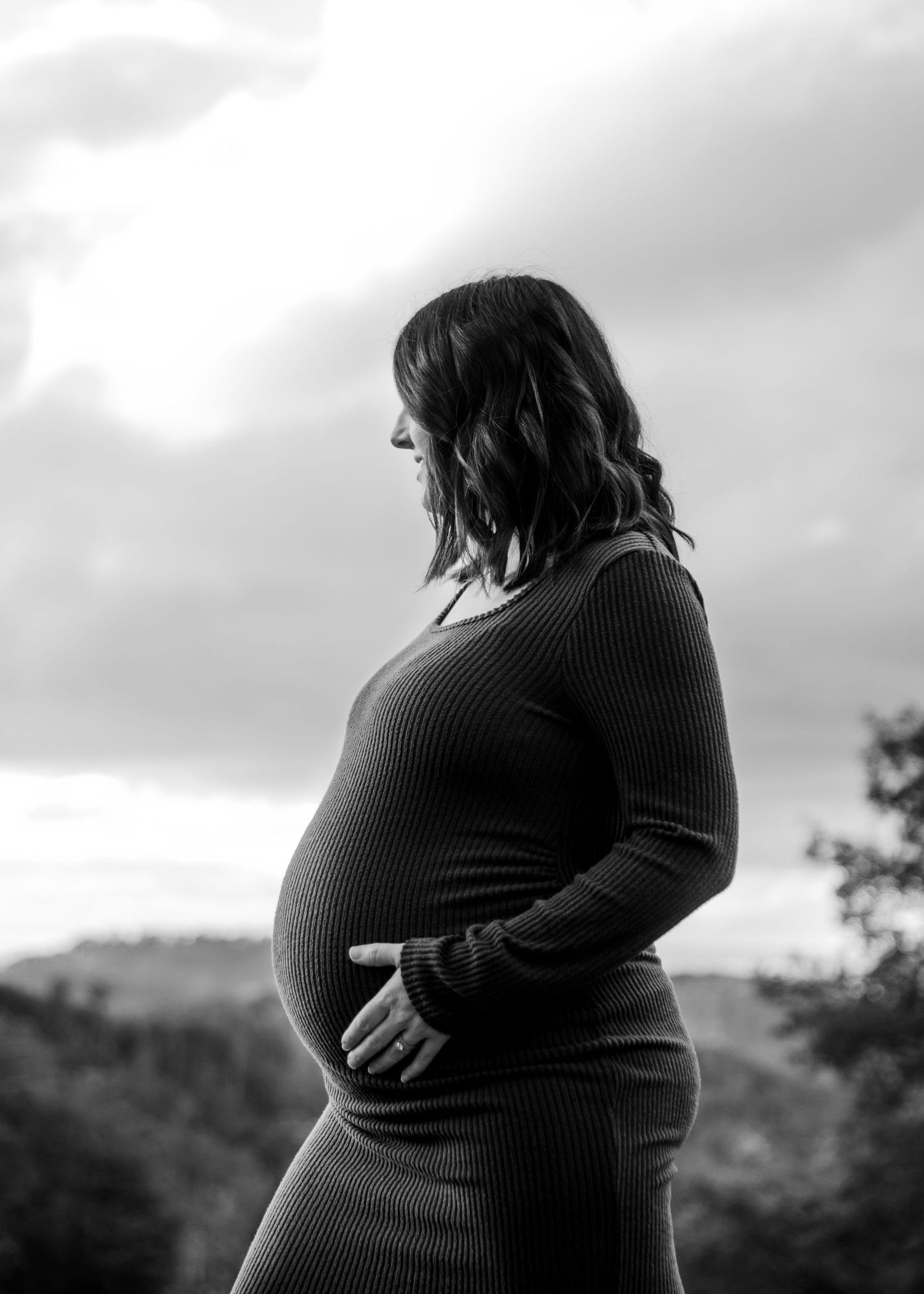 Black and white side profile of pregnant woman holding baby bump outdoors.