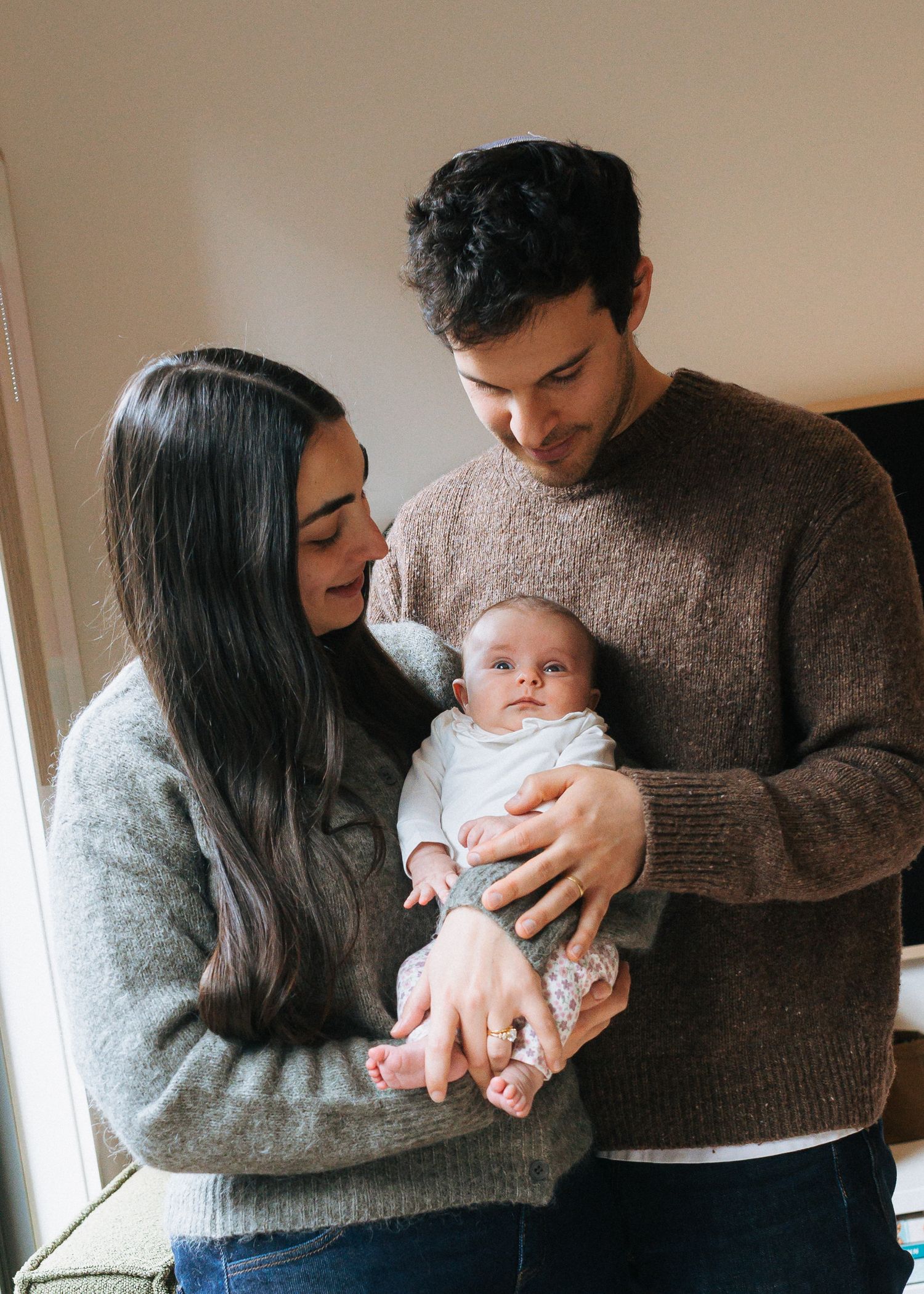 Young parents in cozy sweaters lovingly gazing down at their newborn baby together.