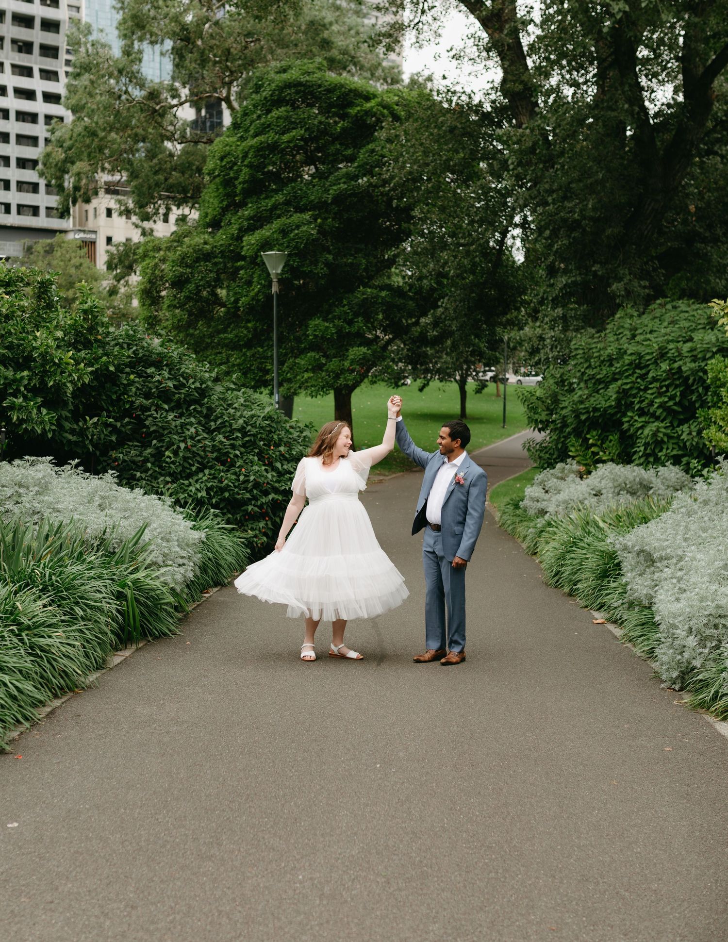 Bride and groom dancing on a garden path, groom spinning bride in a white tulle dress.