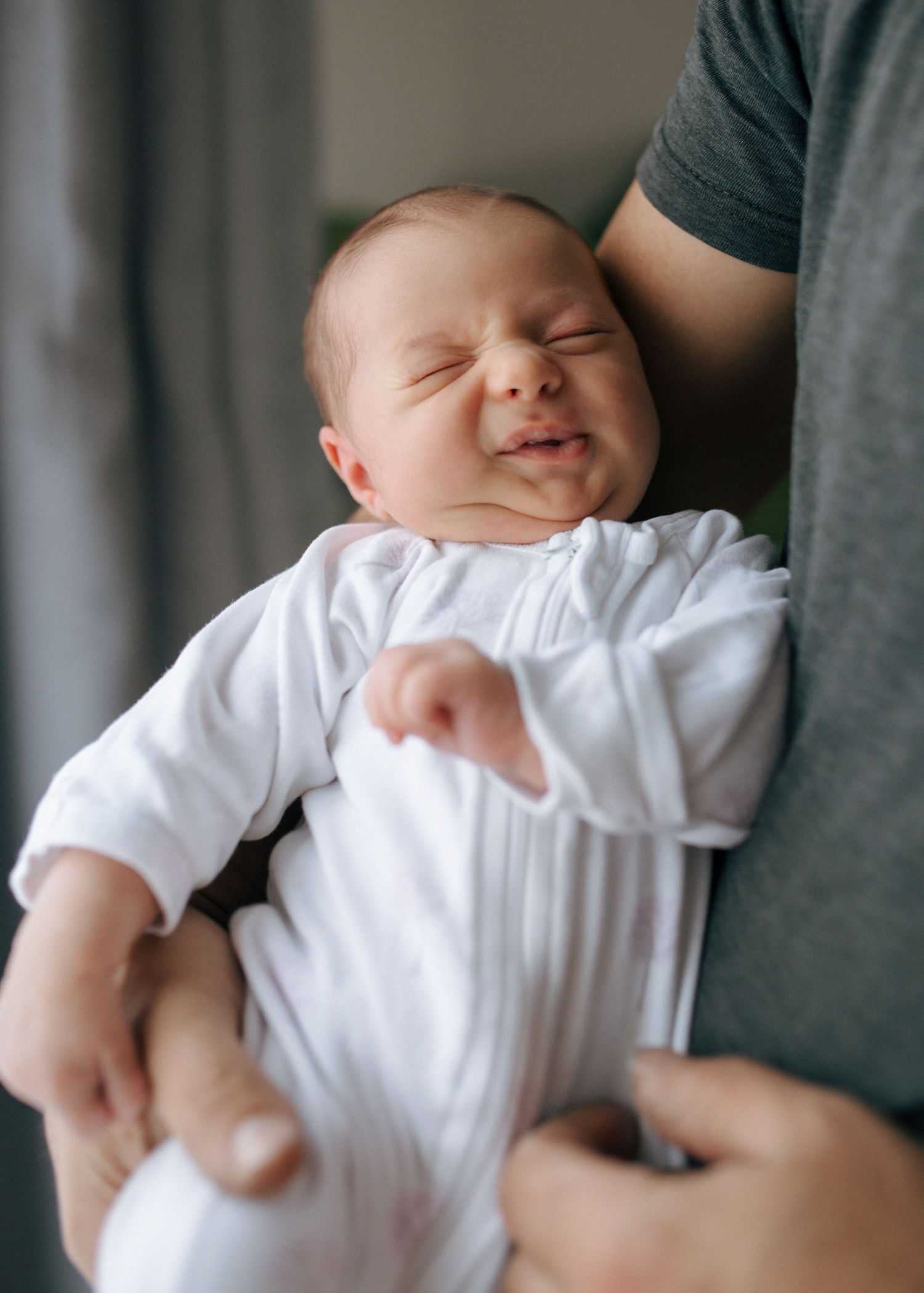 Smiling newborn baby in white outfit being held upright by father.