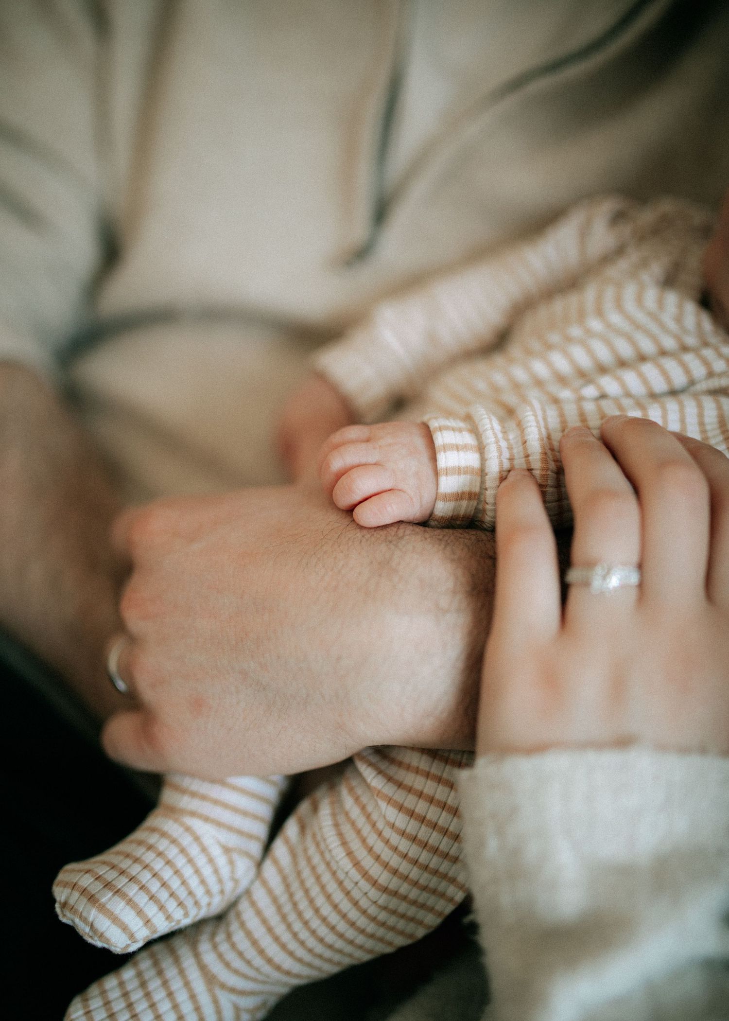 Close-up of a newborn baby's tiny hand resting on parents' hands, wearing a striped onesie.