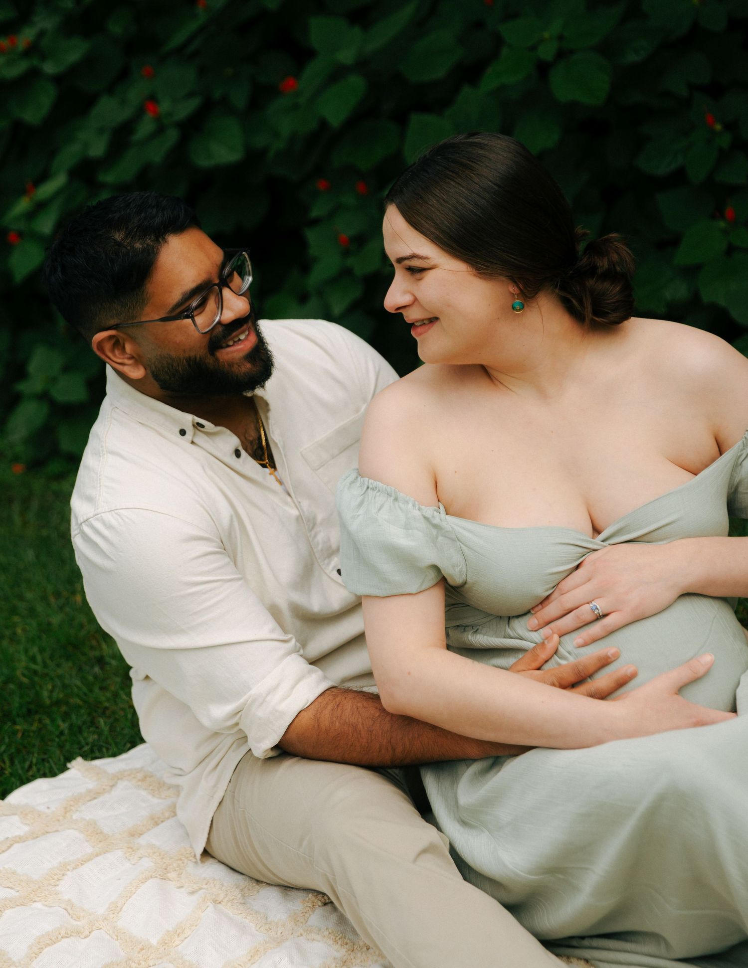 Expecting couple sharing a joyful moment together outdoors, woman in sage maternity dress.