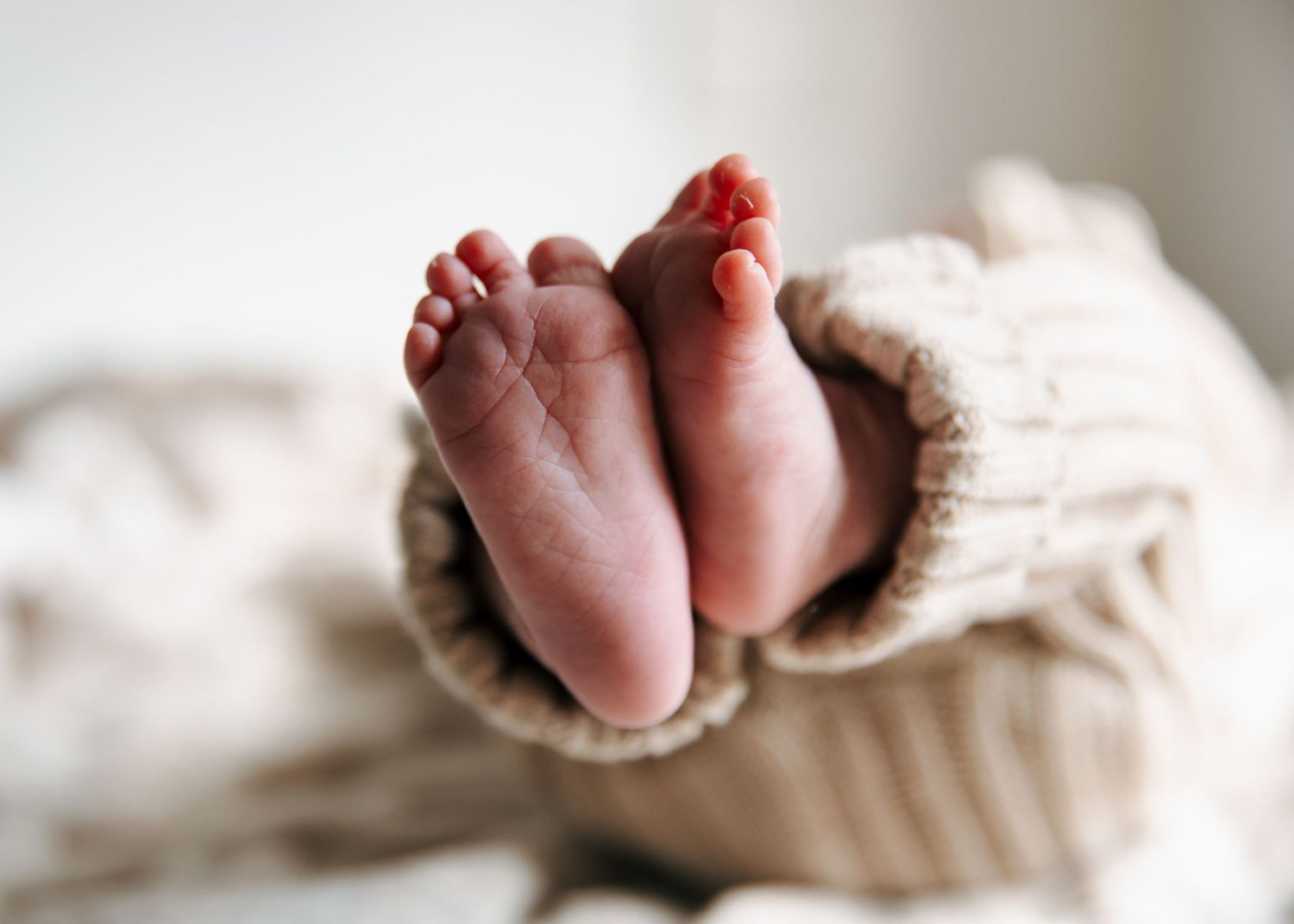 Close-up of tiny newborn baby feet peeking out of a knit romper sleeve.