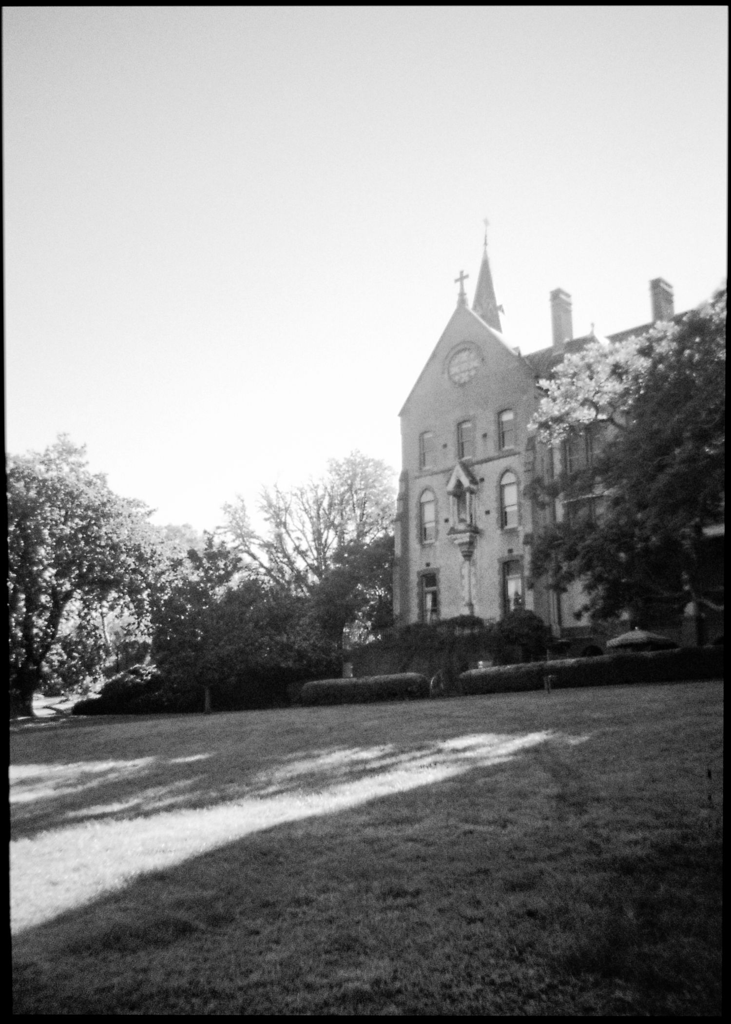 Black and white photo of a historic Gothic stone building with a spire surrounded by trees on a lawn.