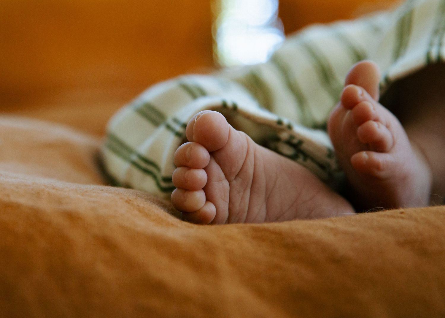 Close-up of newborn baby feet in striped green pants on an orange blanket.